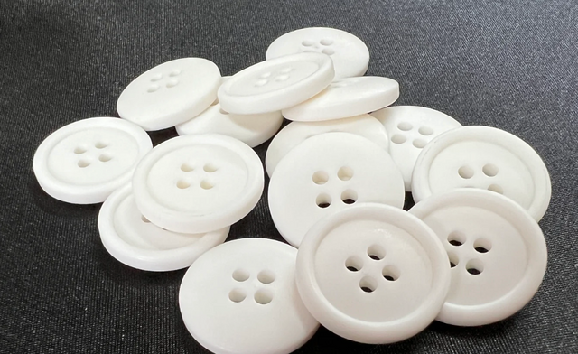 White polyester resin buttons with four holes on a dark fabric background in a pile