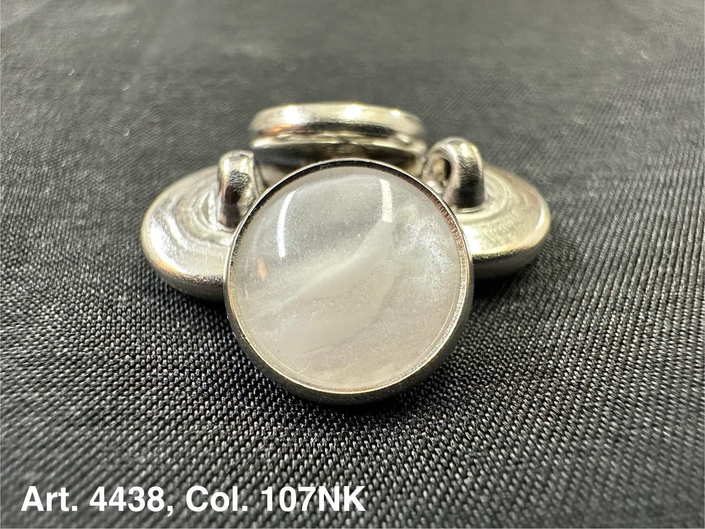 Buttonology Inc polyester garment shank with pearlescent white cabochon and silver metal rim on black fabric
