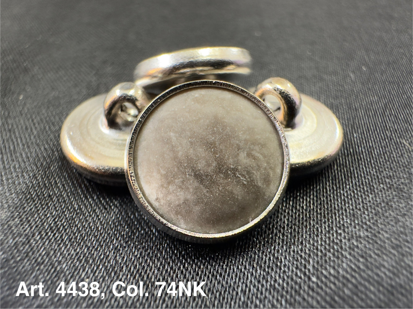 Buttonology Inc polyester garment shank metal button back piece on black woven fabric close up for clothing repairs
