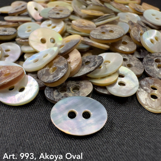Akoya oval buttons in various natural shades with a glossy finish on a dark fabric background