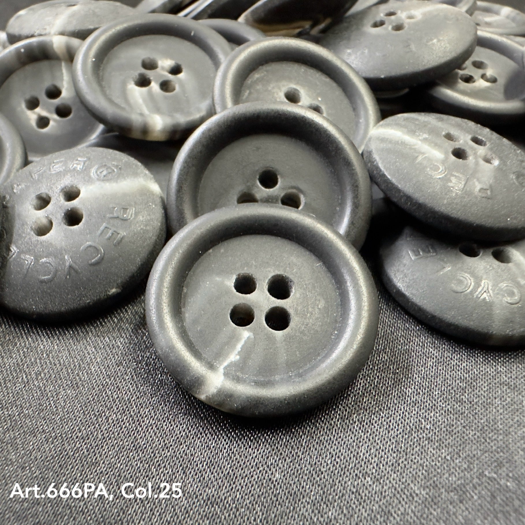 Black recycled paper buttons with four holes displayed on fabric by Buttonology Inc