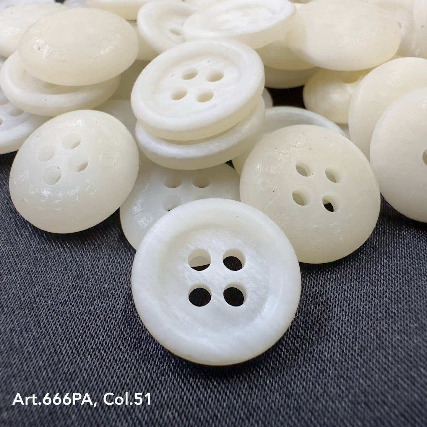 White recycled paper buttons from Buttonology Inc with four holes on dark fabric background