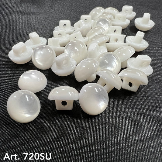 Buttonology Inc white pearl round shank buttons for garments scattered on dark denim fabric