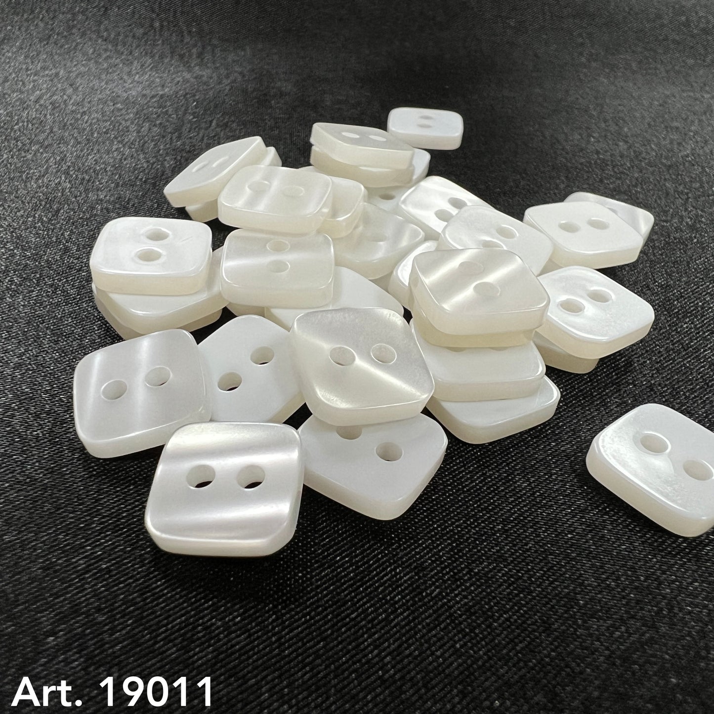 Square pearl buttons by Buttonology Inc in a pile on black fabric background