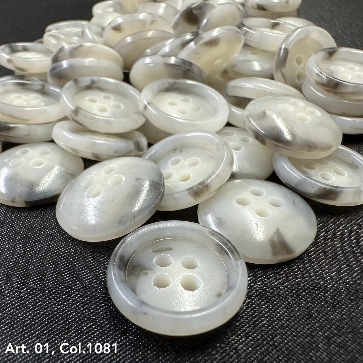 Buttonology Inc white pearlescent four hole round buttons scattered on dark fabric premium shirt buttons for sewing