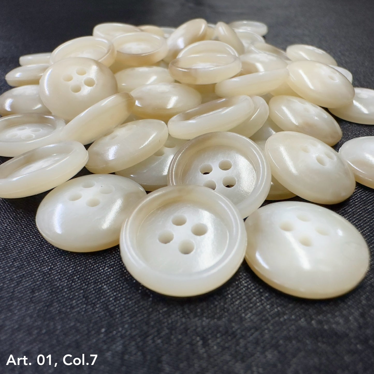 Buttonology Inc pearl white four hole round buttons piled on dark fabric premium shirt buttons for sewing
