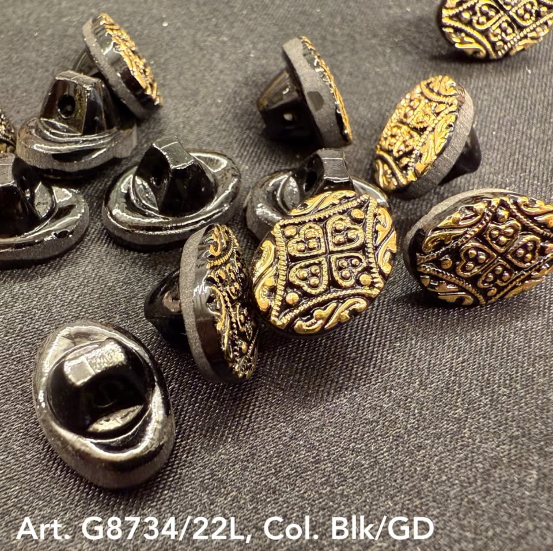 Black and gold decorative buttons with intricate embossed design on black fabric surface