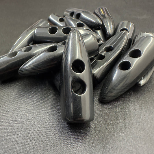 Black toggle buttons from Buttonology Inc with two holes on a black surface
