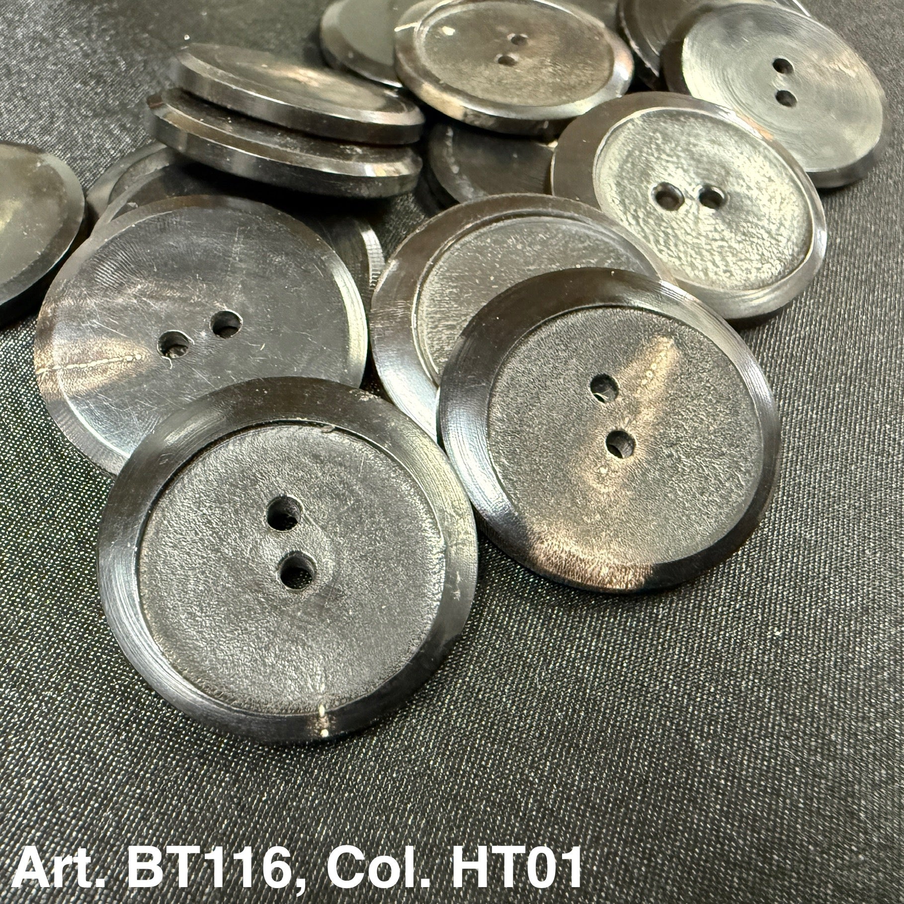 Buttonology Inc pile of glossy gray black round two hole buttons on dark fabric premium horn button 2-hole