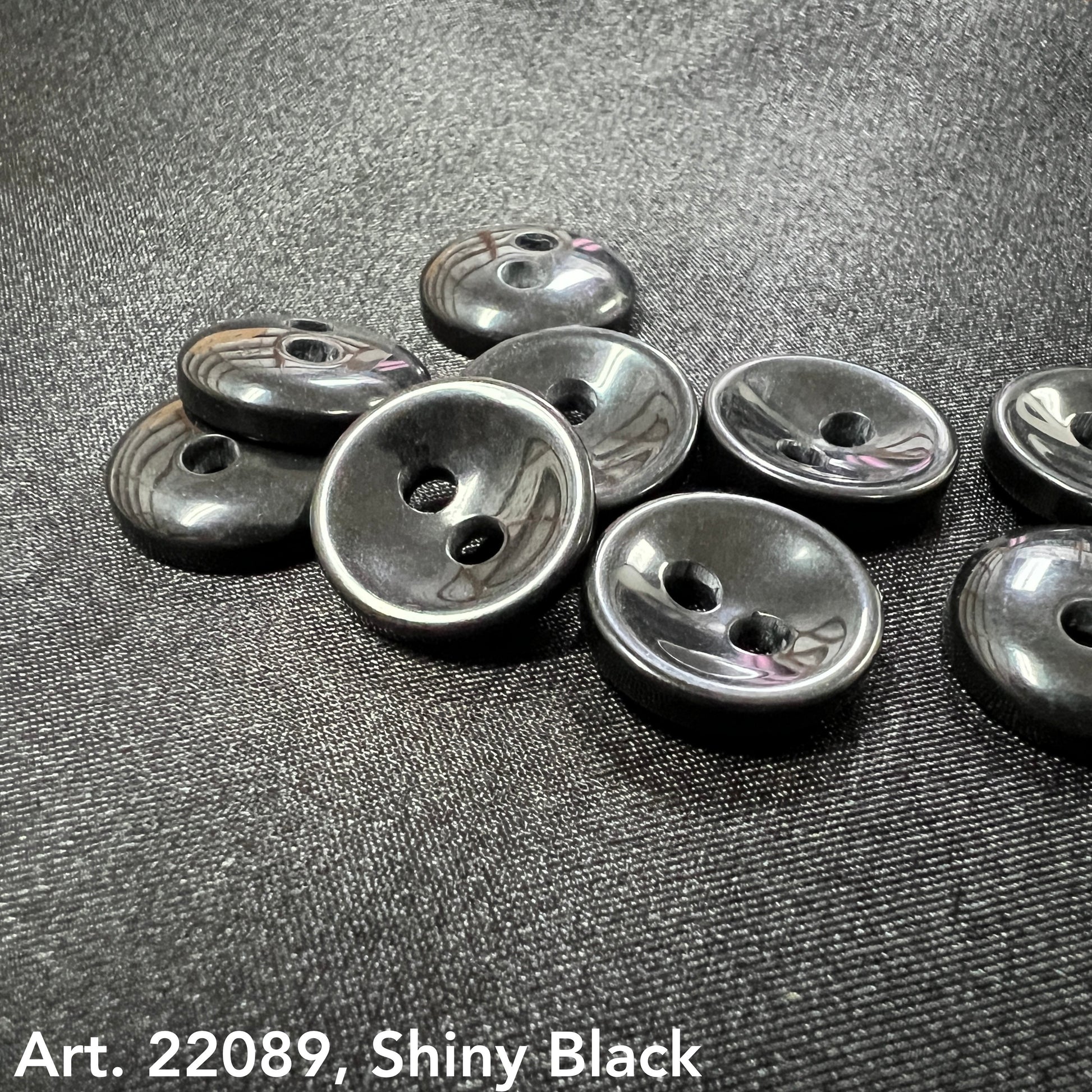Shiny black two hole round buttons on textured black fabric by Buttonology Inc buy shiny black buttons online