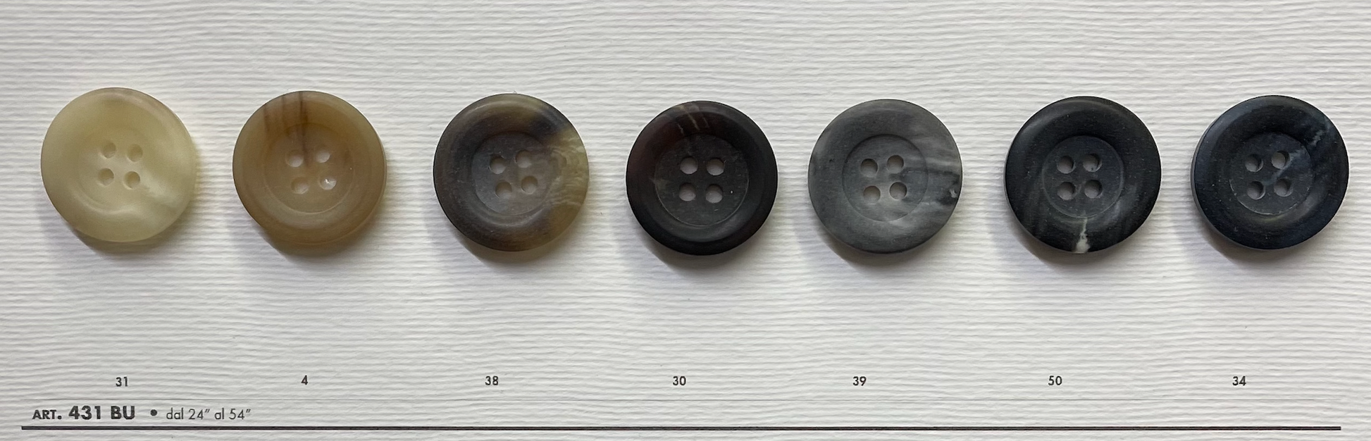 Collection of assorted colored buttons for sale by Buttonology Inc arranged in a row on white background