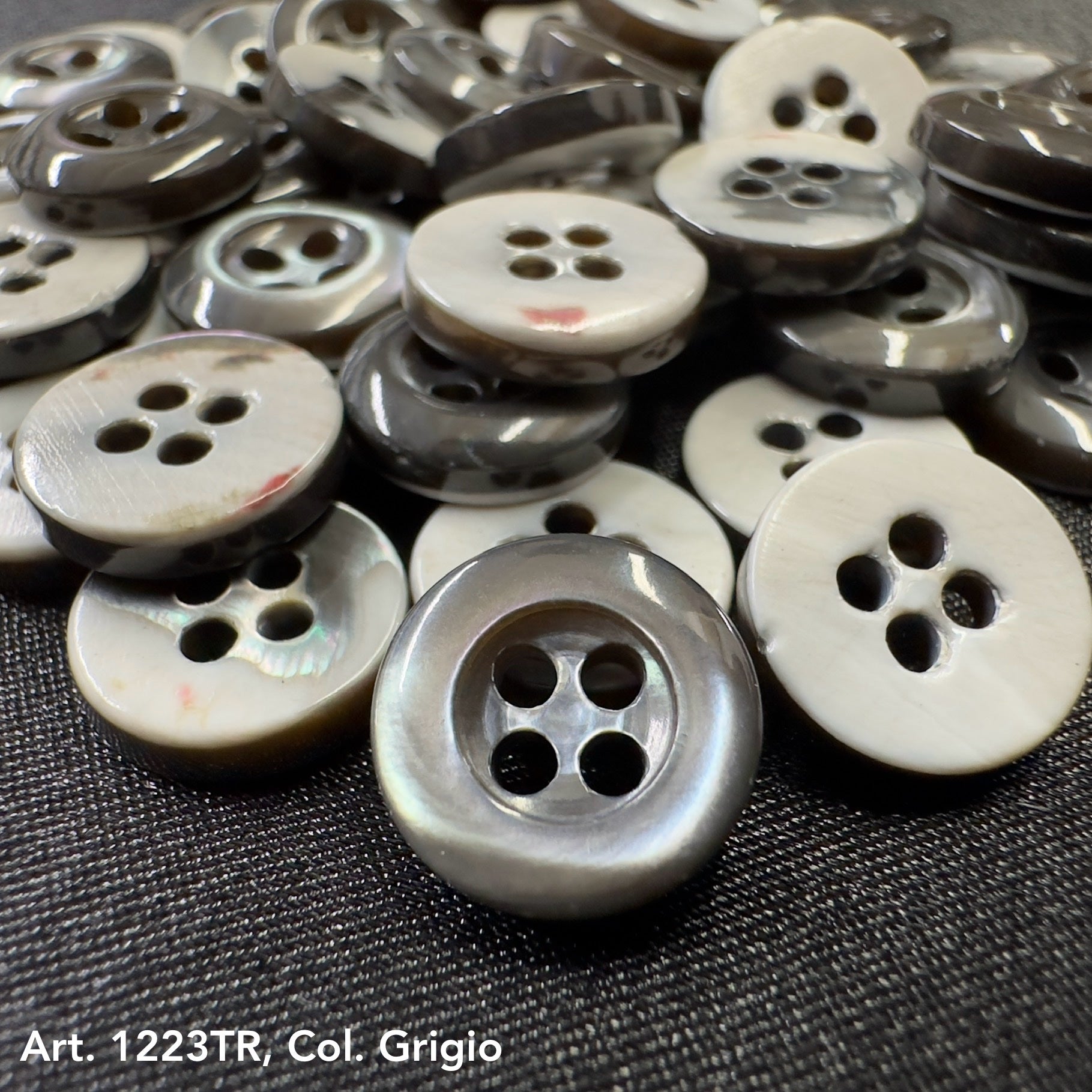 Gray and white shell buttons stacked on black fabric buy shell buttons online from Buttonology Inc