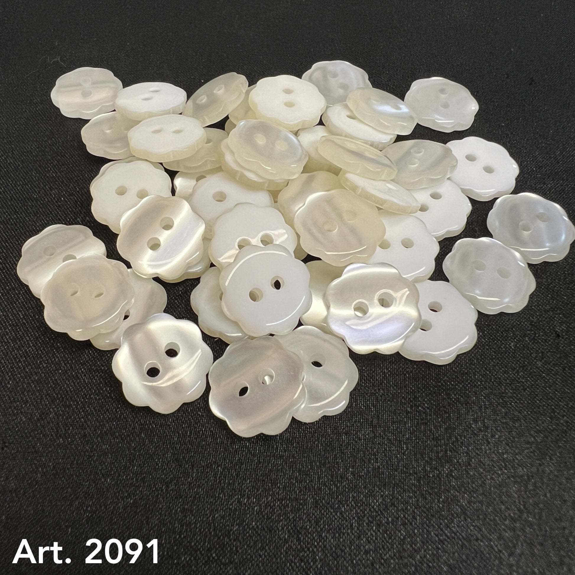 Buttonology Inc custom flower buttons in pearly white with two holes laid on black fabric background