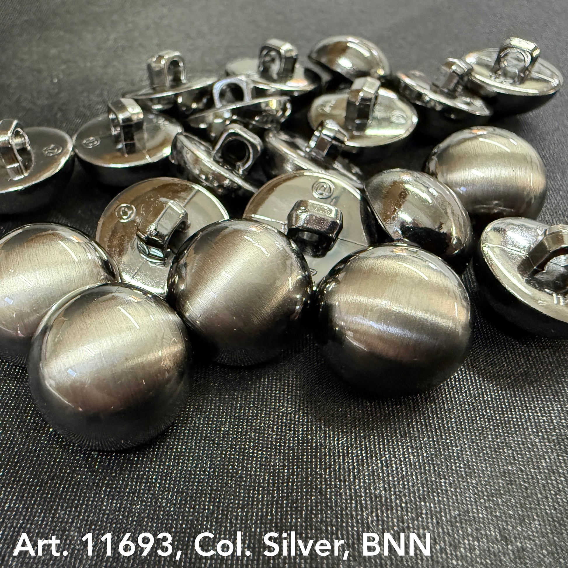Designer clothes buttons silver by Buttonology Inc laid out on black fabric showing shiny round metal buttons