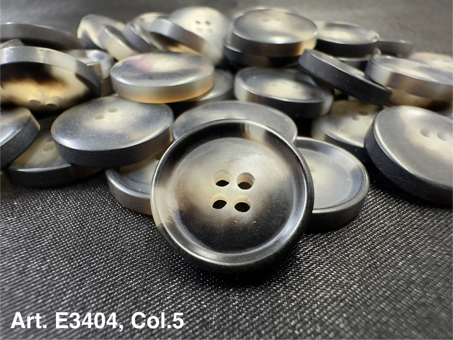 Buttonology Inc grey round plastic four hole sewing buttons stacked on fabric showing matte and glossy finishes