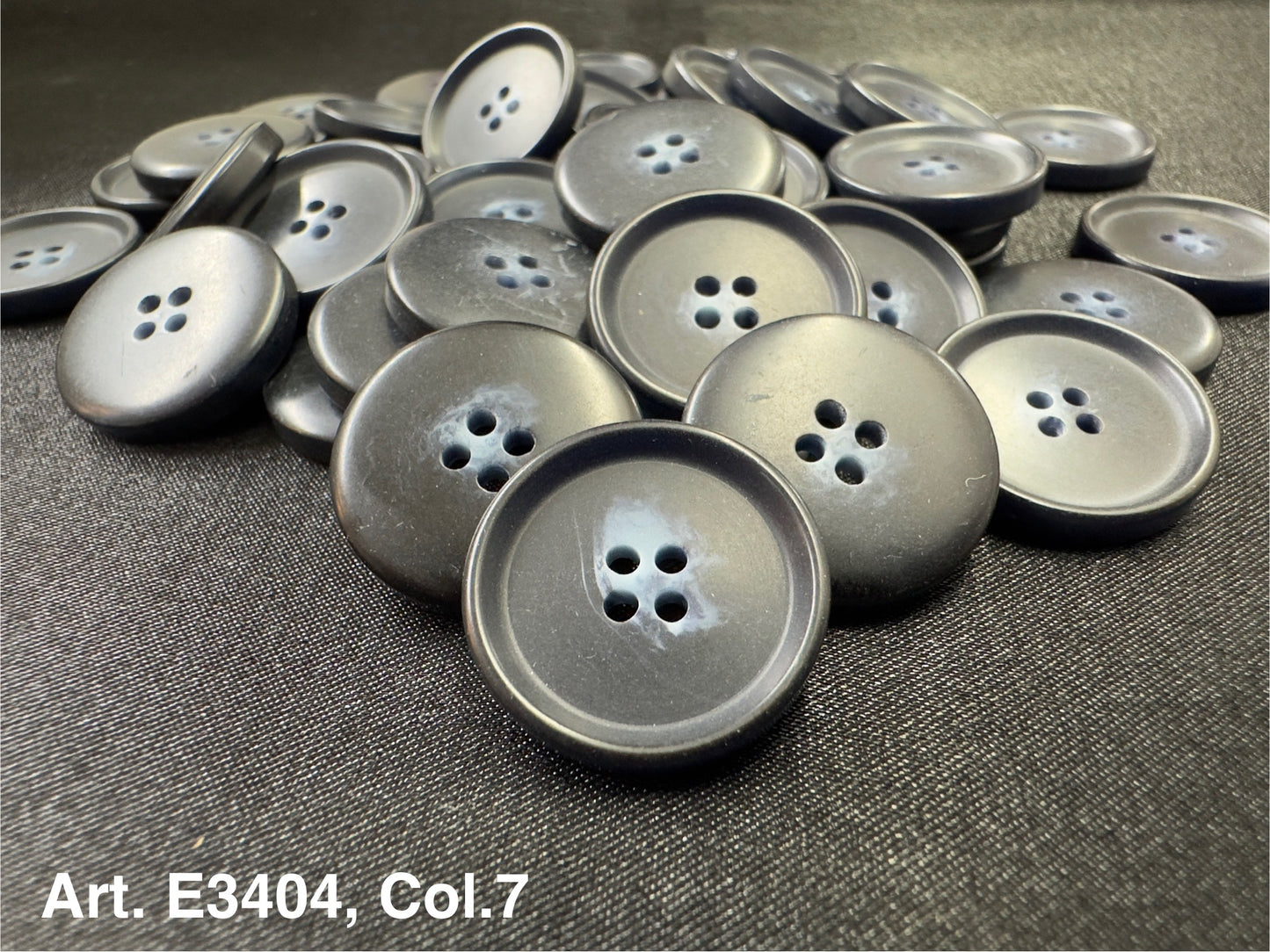 Buttonology Inc matte black plastic four hole sewing buttons piled on black fabric for garments