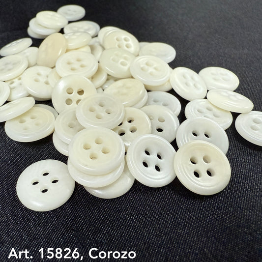 Pile of white Corozo buttons from Buttonology Inc, an eco-friendly button supplier on black fabric background