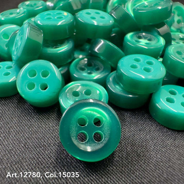 Green 18L four hole plastic buttons by Buttonology Inc arranged on dark fabric background