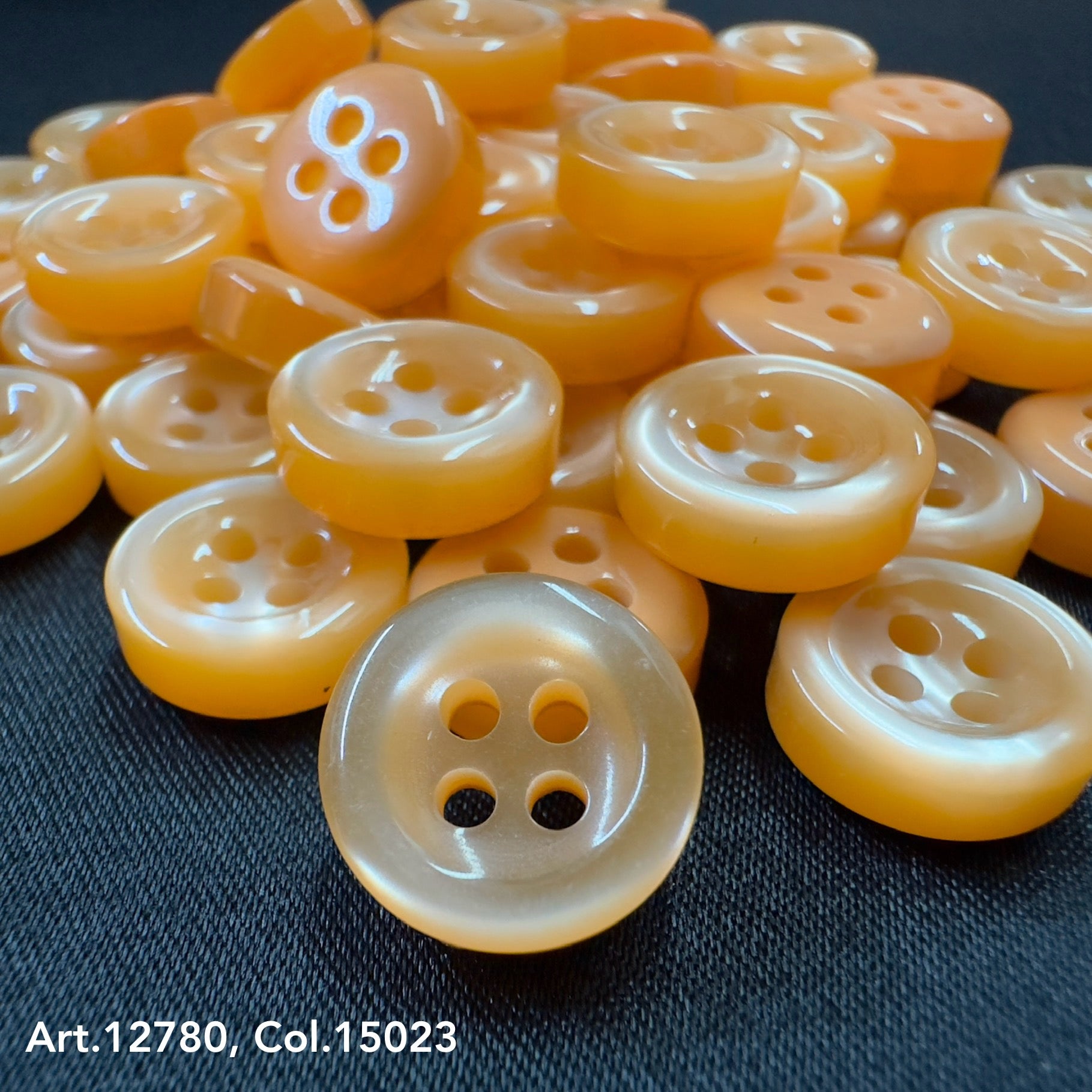 18L four hole plastic buttons in translucent orange by Buttonology Inc neatly arranged on dark fabric