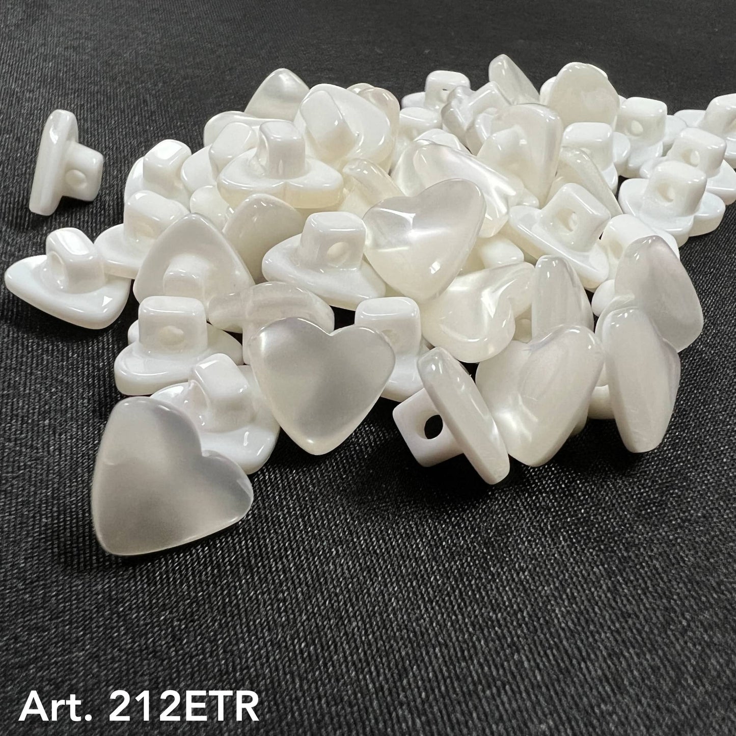 White pearl heart-shaped garment buttons from Buttonology Inc. spread on black fabric