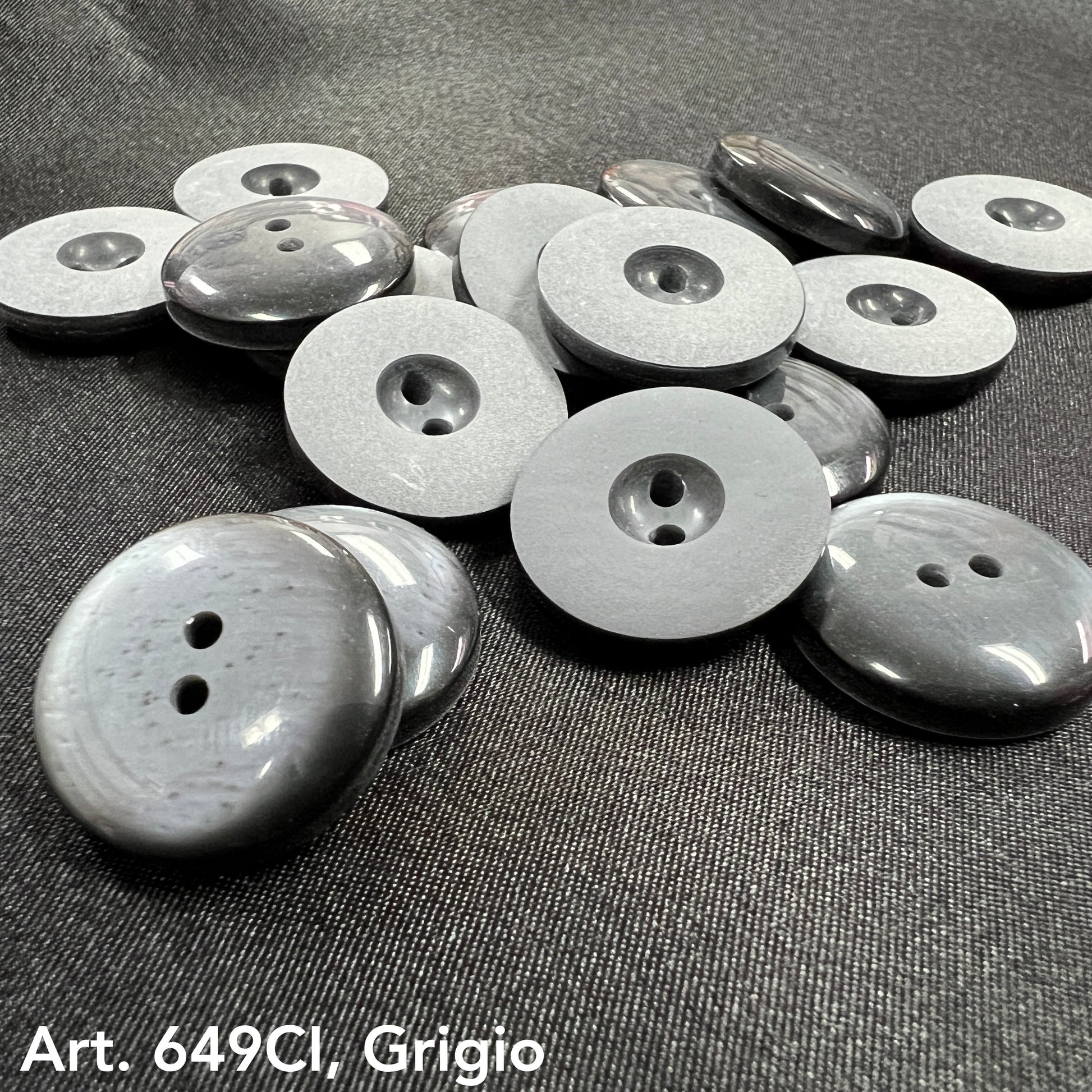High-quality sewing buttons in gray by Buttonology Inc spread on black fabric