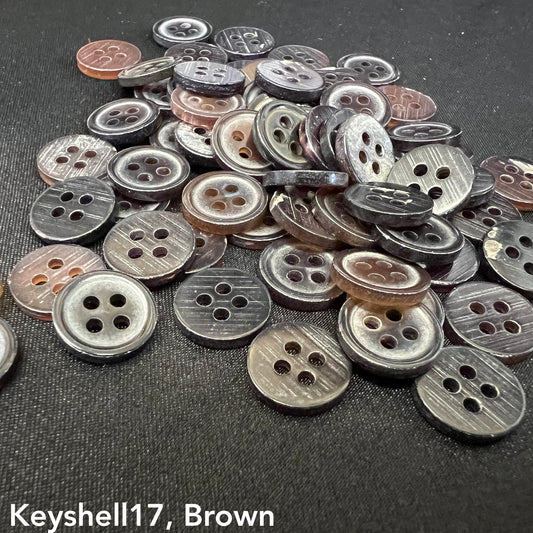 Key Shell Shape 17 buttons in mixed brown and gray tones scattered on black fabric from Buttonology Inc