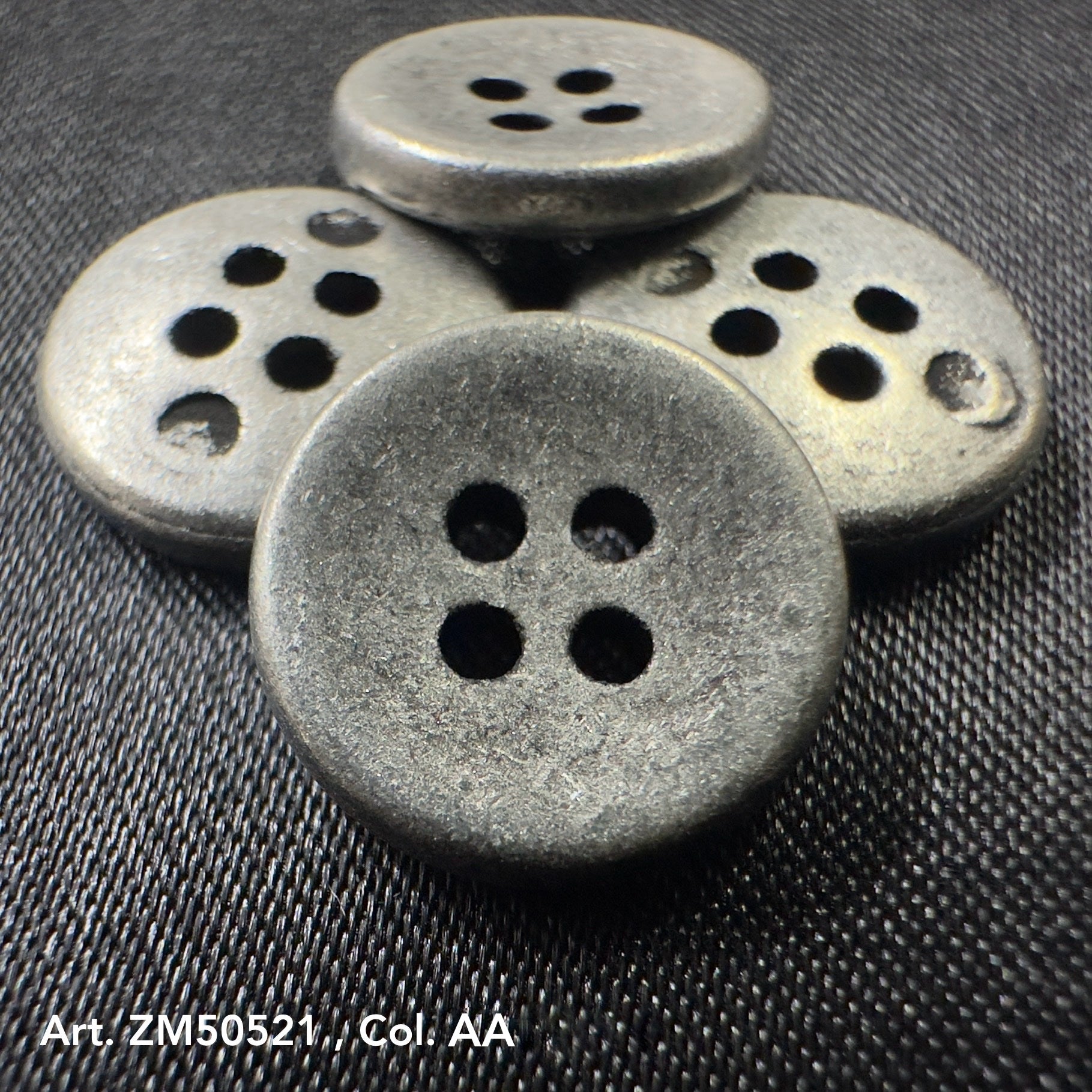 Set of four round metal buttons for clothes with a matte finish and four holes on dark fabric