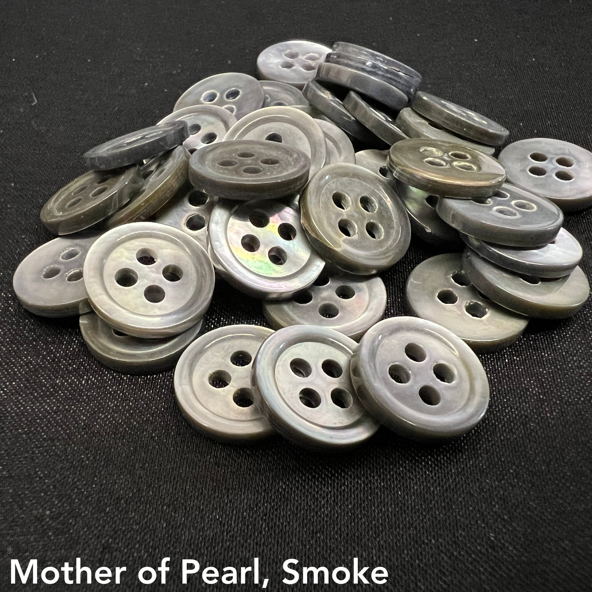 Pile of gray and black mother of pearl buttons with four holes by Buttonology Inc on black fabric