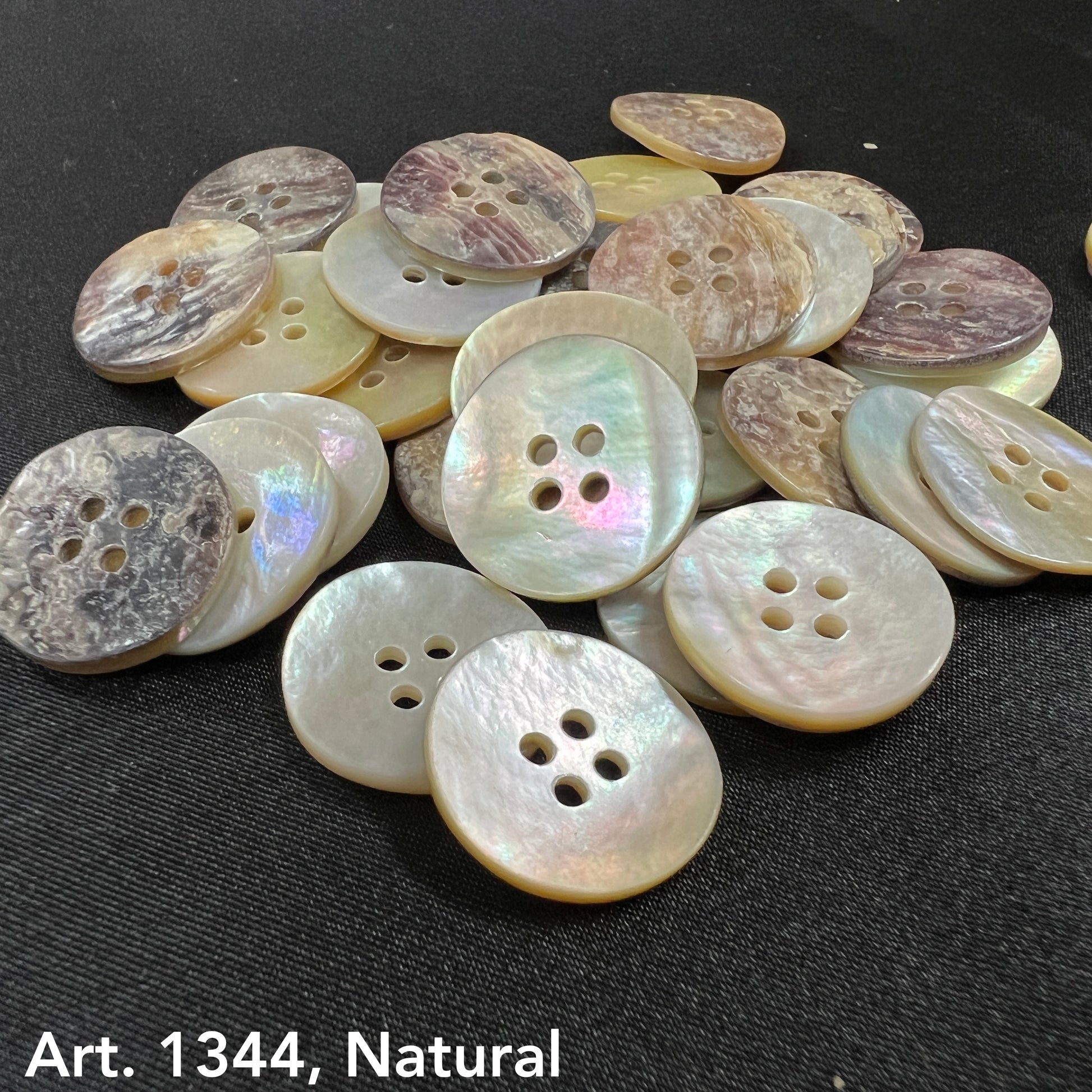 Natural Akoya buttons by Buttonology Inc displayed on black fabric with pearlescent and earthy tones