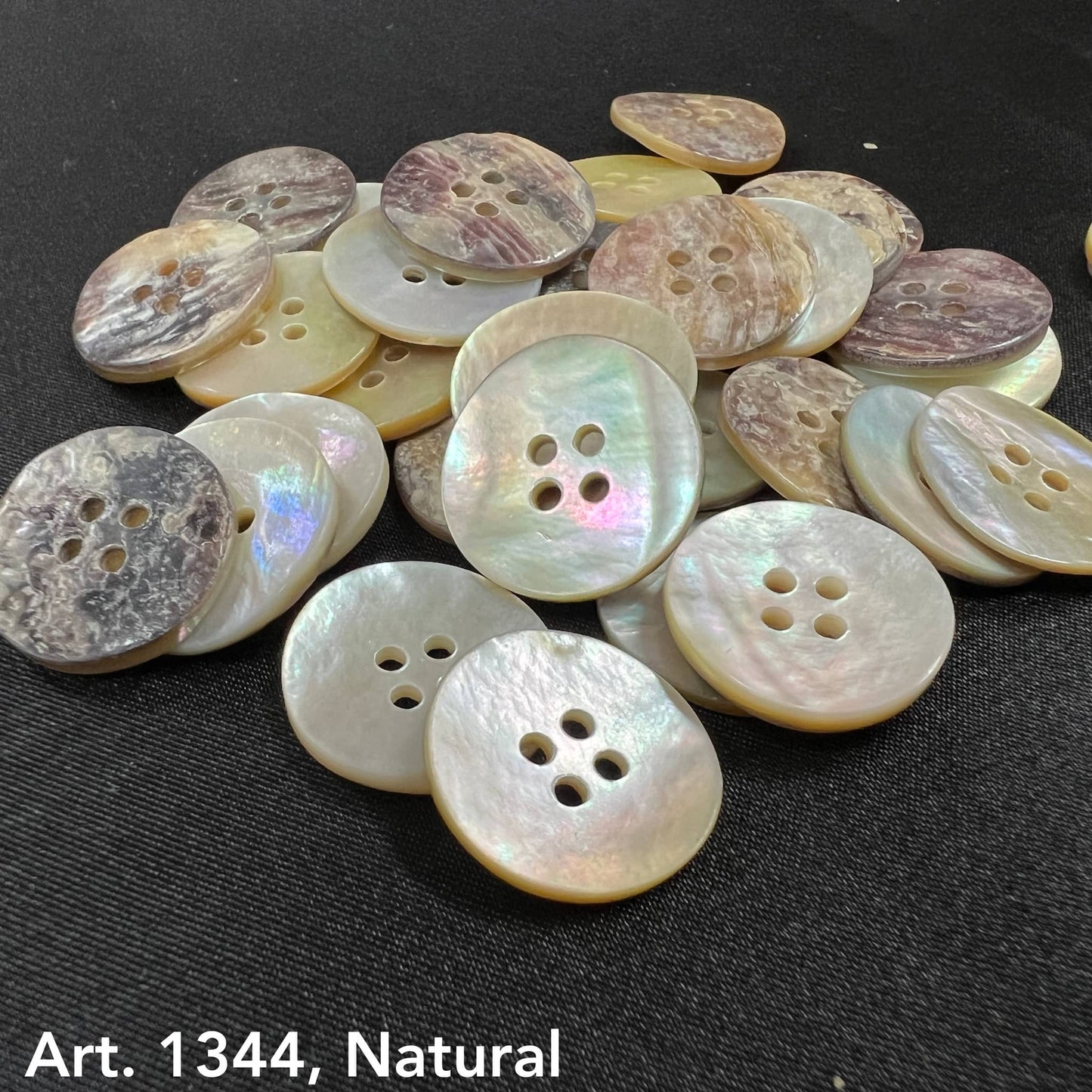 Natural Akoya buttons by Buttonology Inc displayed on black fabric with pearlescent and earthy tones