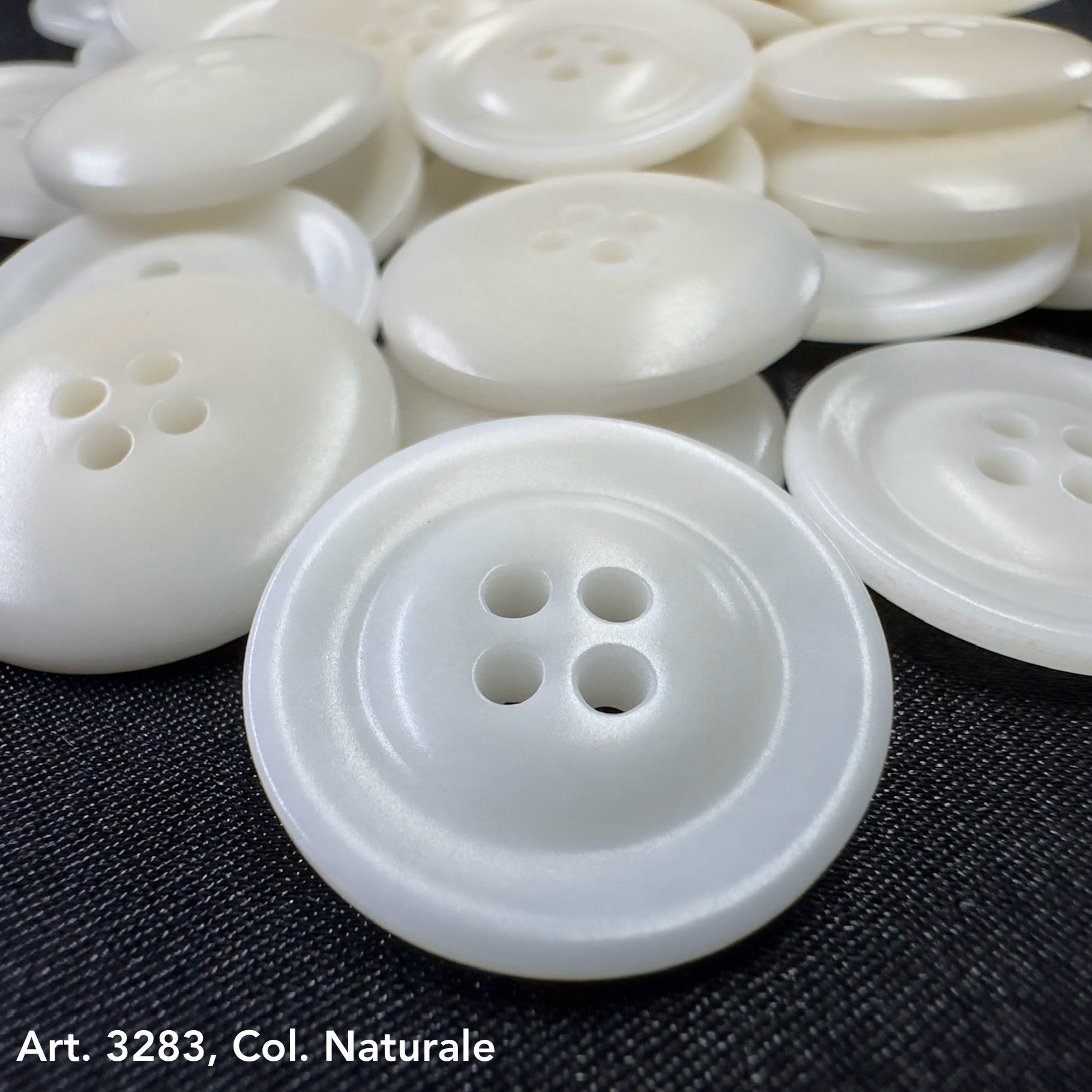 White eco-friendly garment buttons with four holes on dark fabric by Buttonology Inc