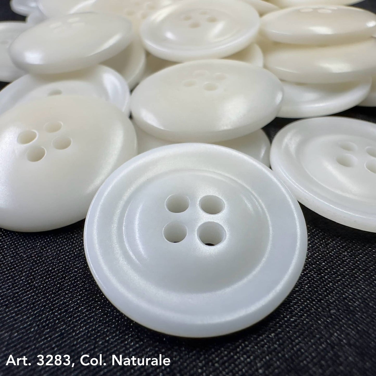 White eco-friendly garment buttons with four holes on dark fabric by Buttonology Inc