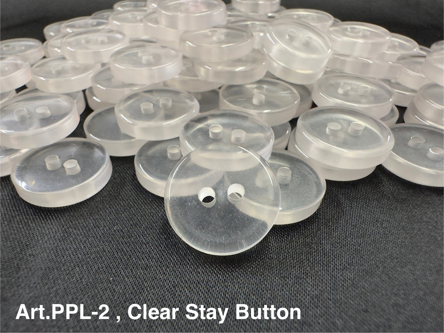 Buttonology Inc clear stay button 2-hole translucent round sewing buttons piled on black fabric