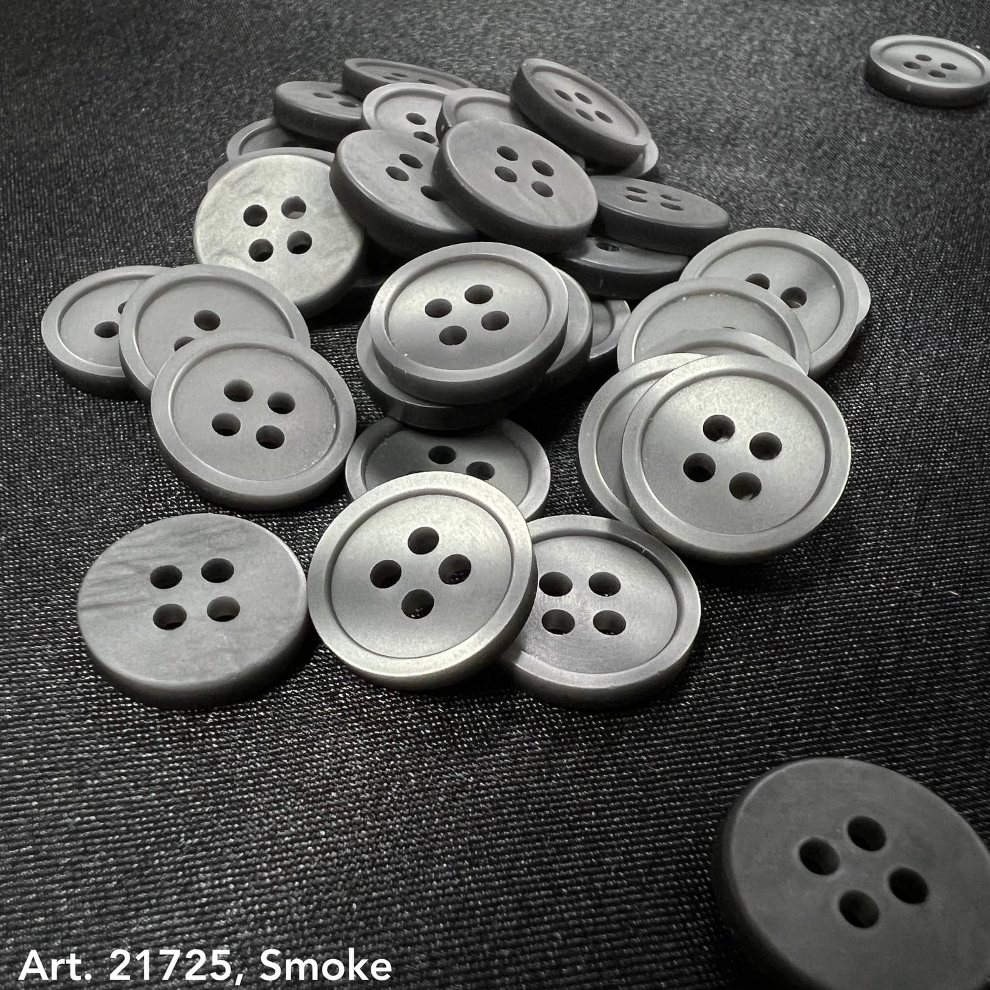 Premium button collection by Buttonology Inc featuring smoke gray four-hole buttons on dark fabric