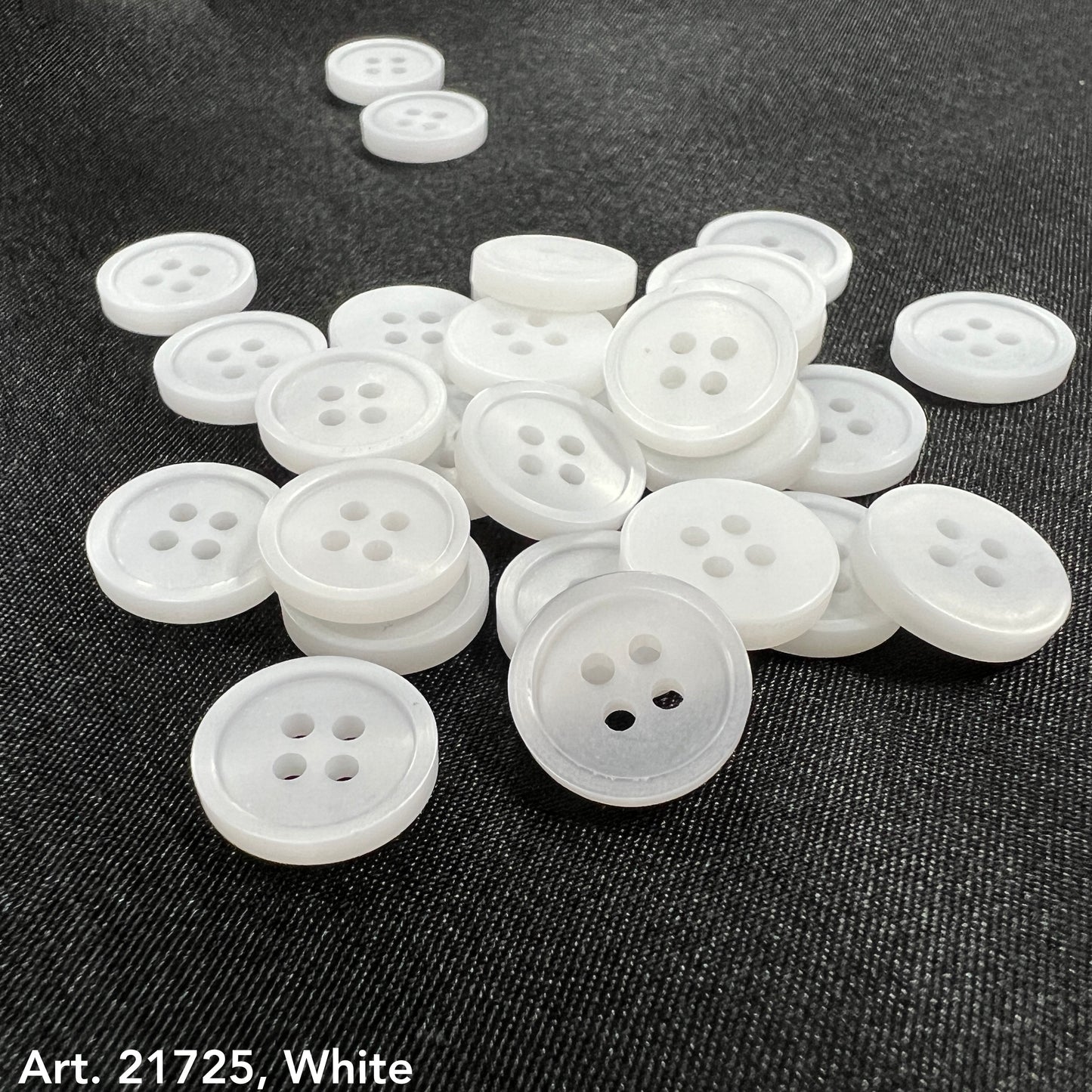 White buttons from the premium button collection by Buttonology Inc spread on dark fabric background