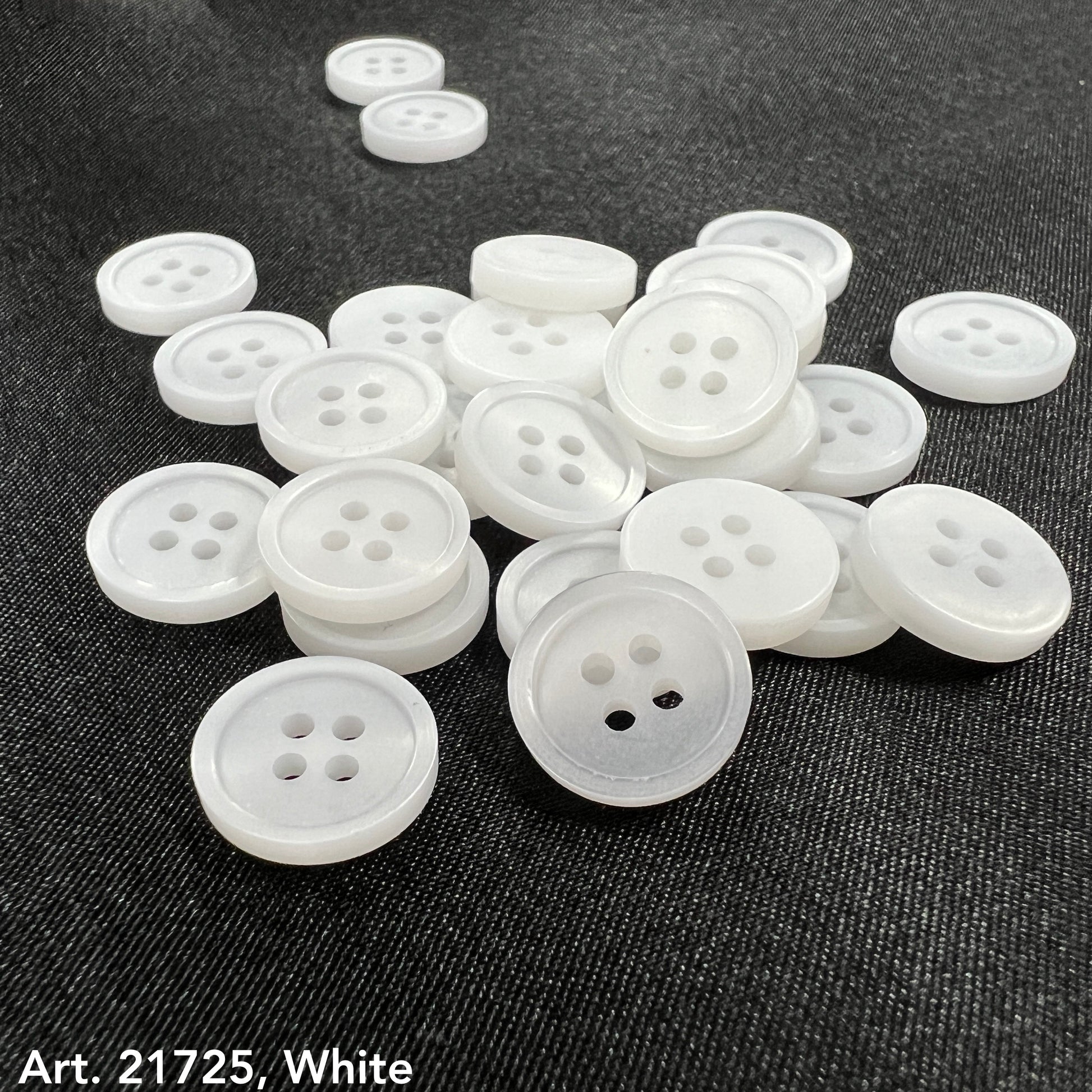 White buttons from the premium button collection by Buttonology Inc spread on dark fabric background