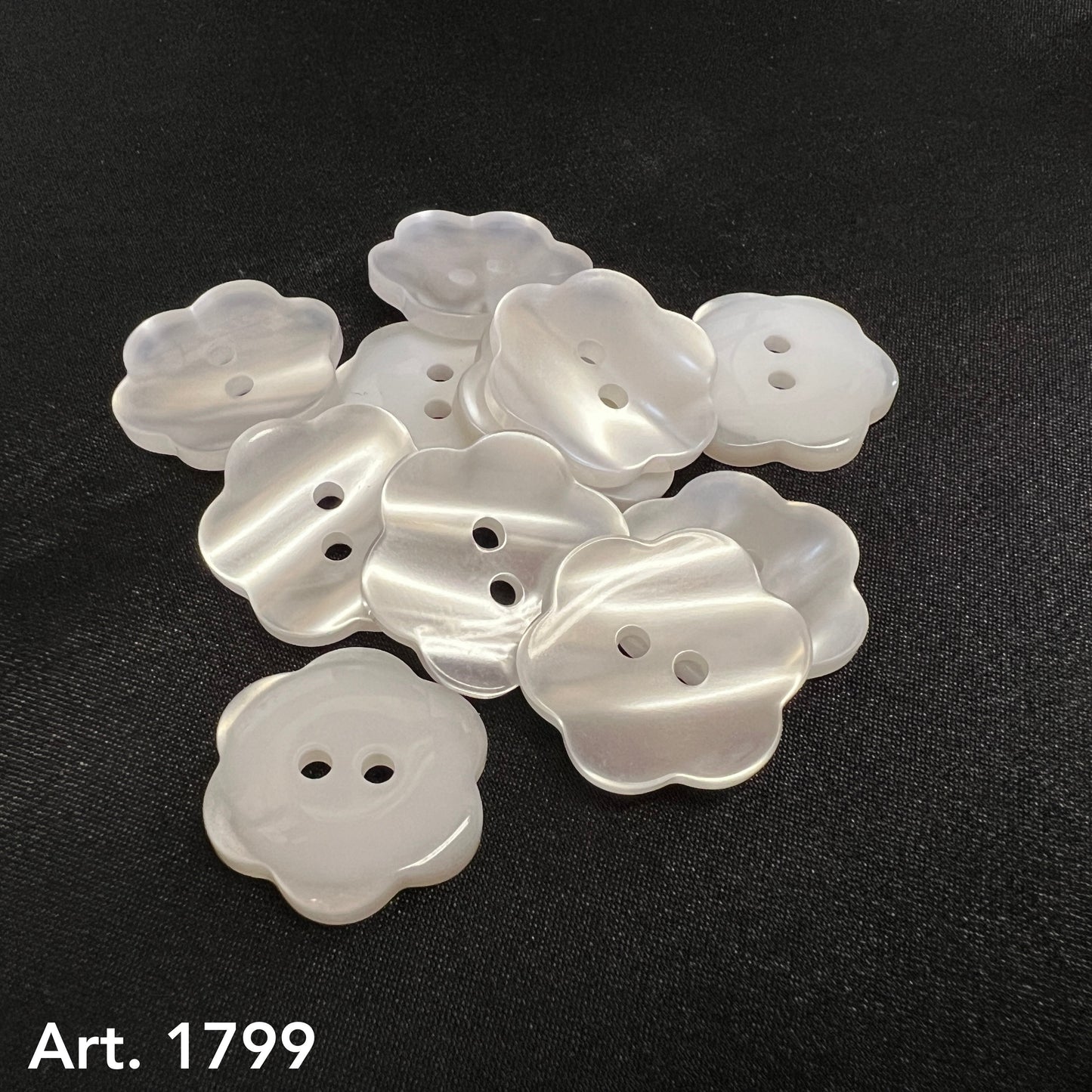 Buttonology Inc premium flower-shaped buttons in pearly white arranged on black fabric background