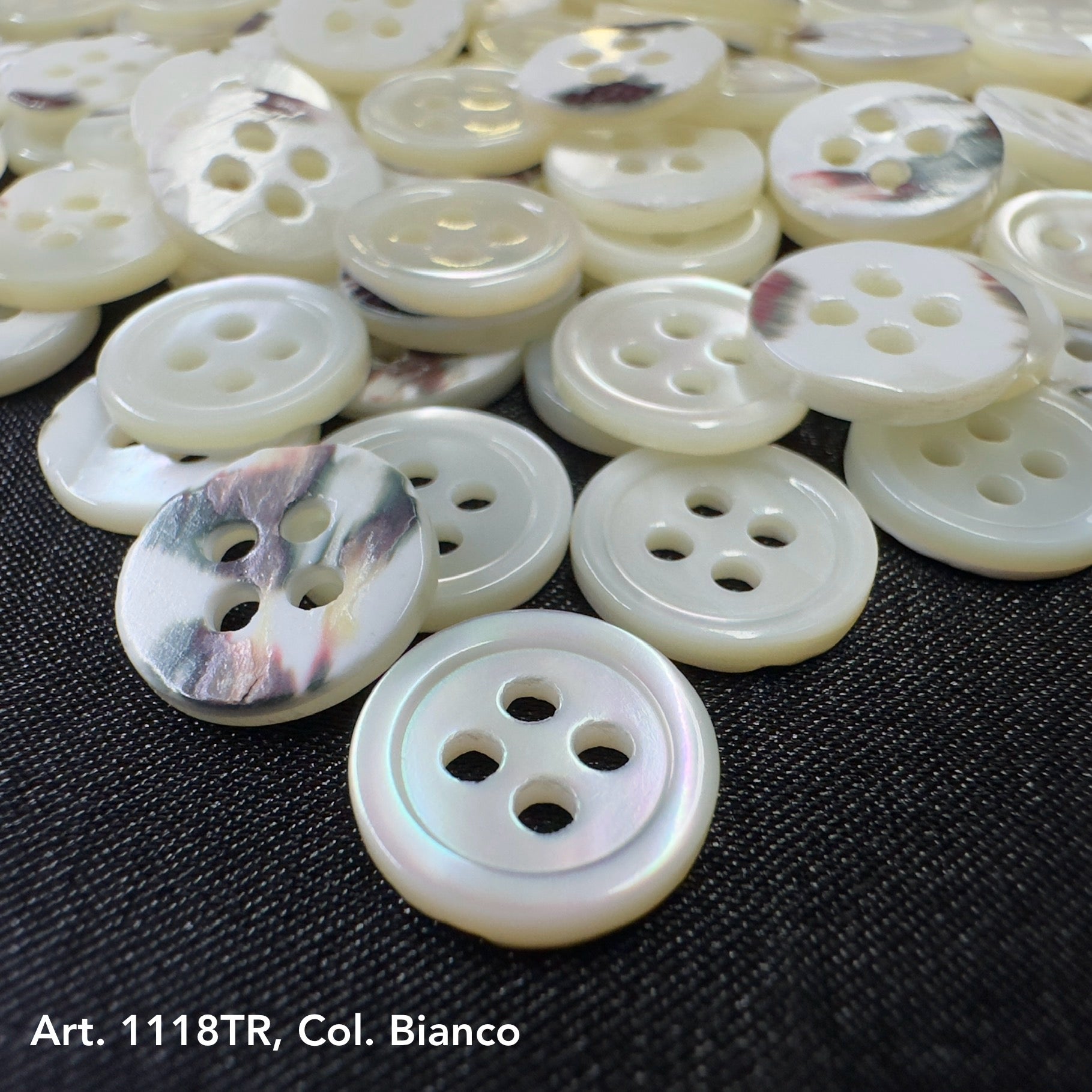 Premium shell sewing buttons in white with four holes from Buttonology Inc displayed on black fabric