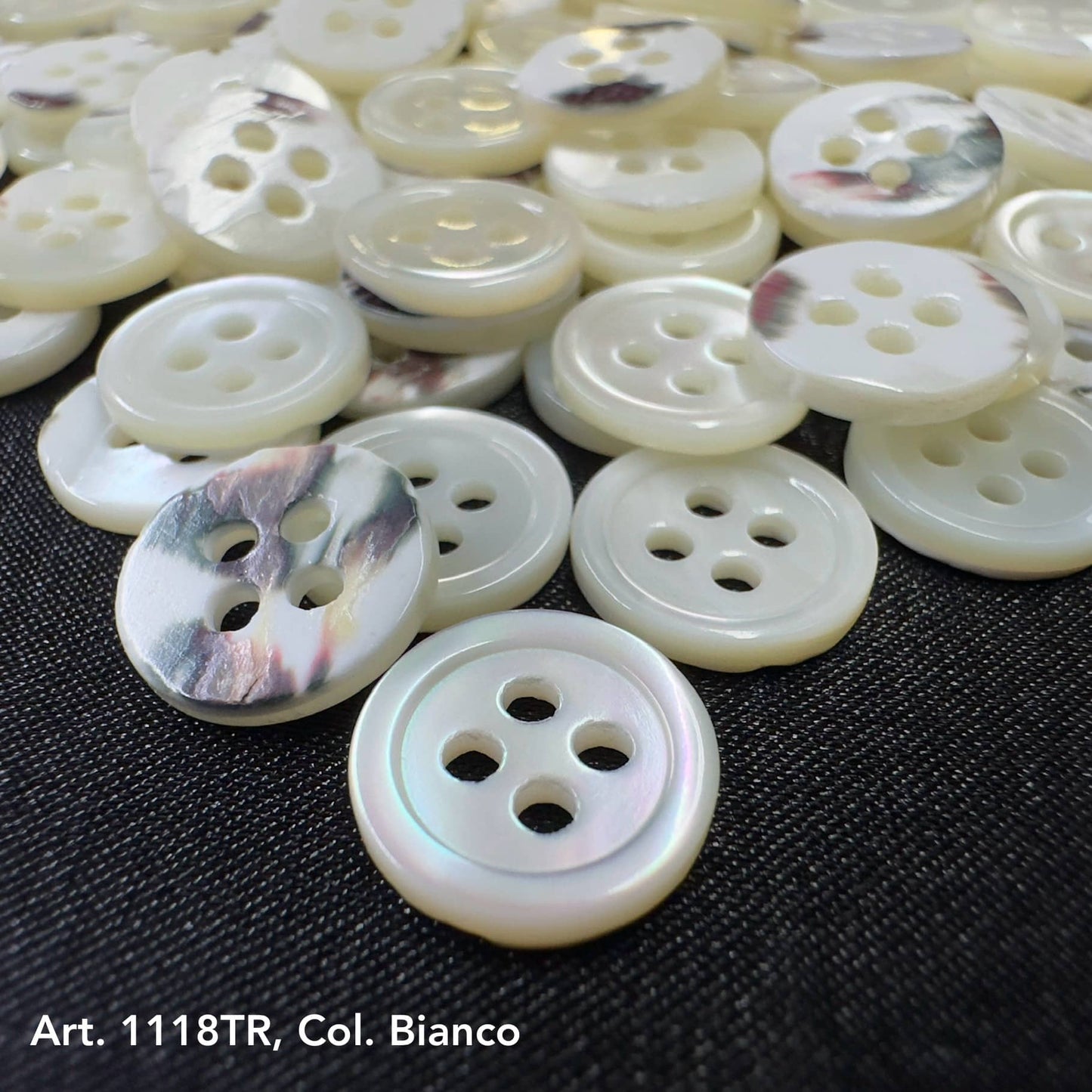 Premium shell sewing buttons in white with four holes from Buttonology Inc displayed on black fabric