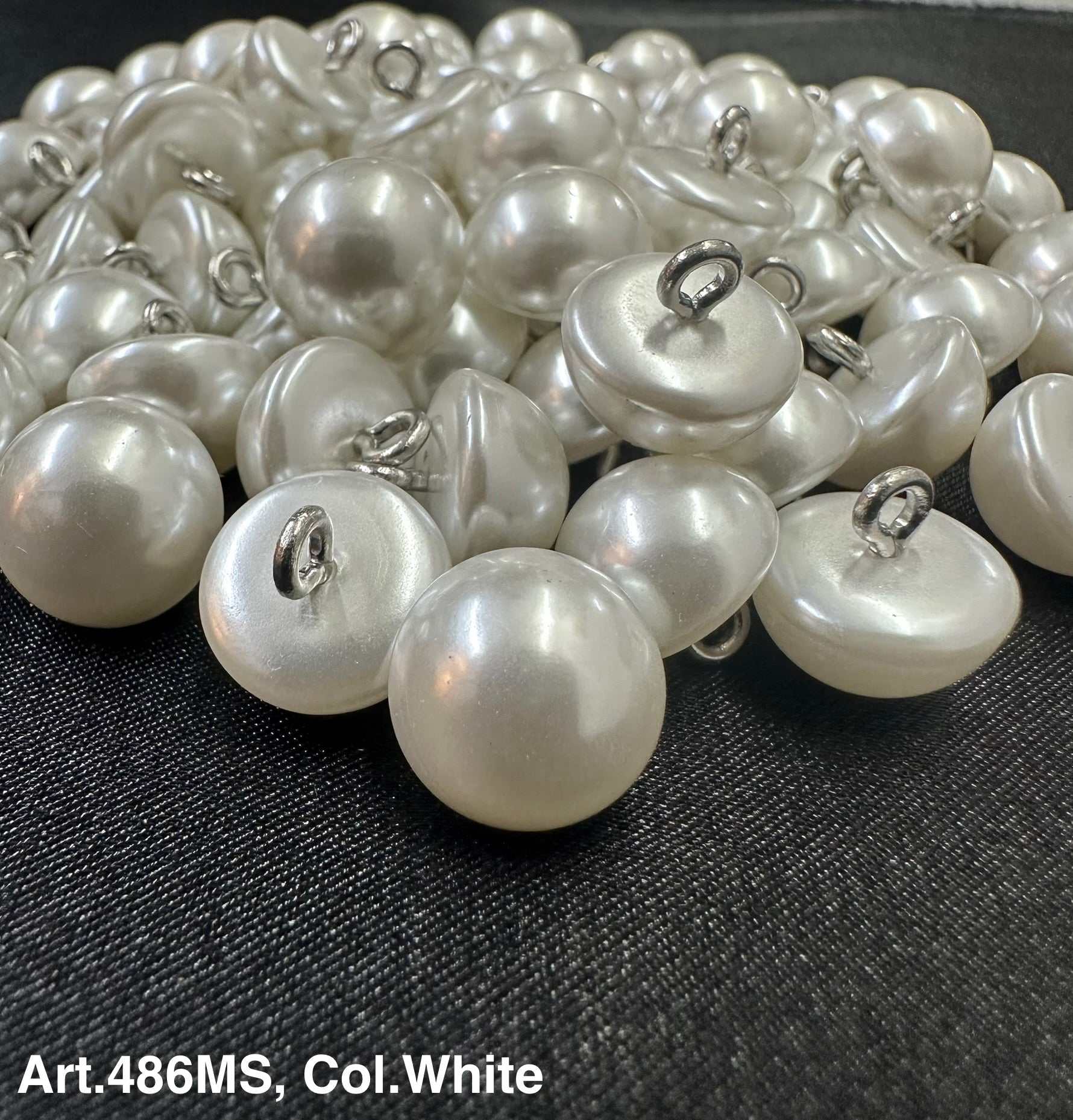 Buttonology Inc white pearl shank buttons piled on fabric showing glossy dome pearls with metal shanks for sewing