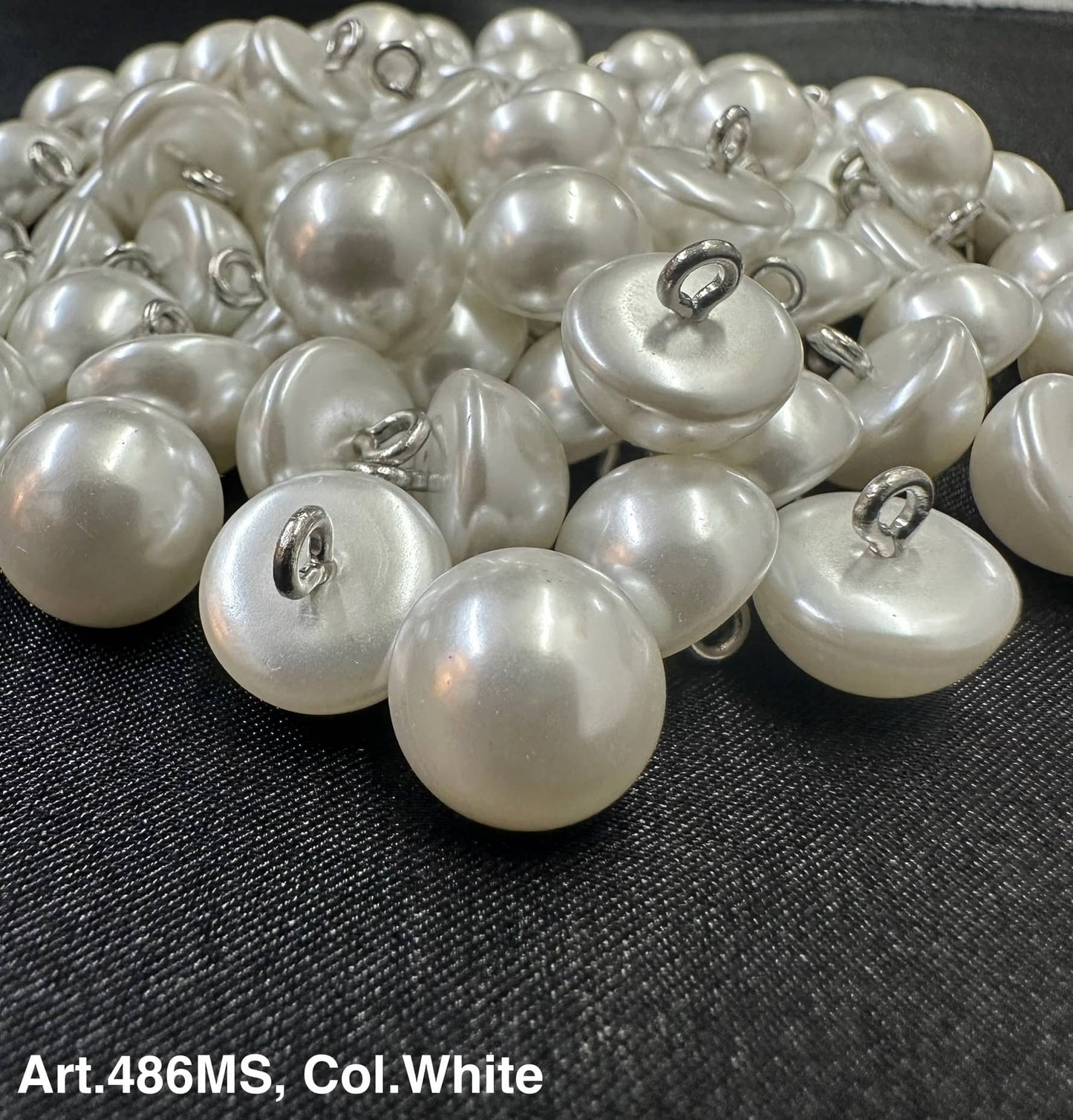 Buttonology Inc white pearl shank buttons piled on fabric showing glossy dome pearls with metal shanks for sewing