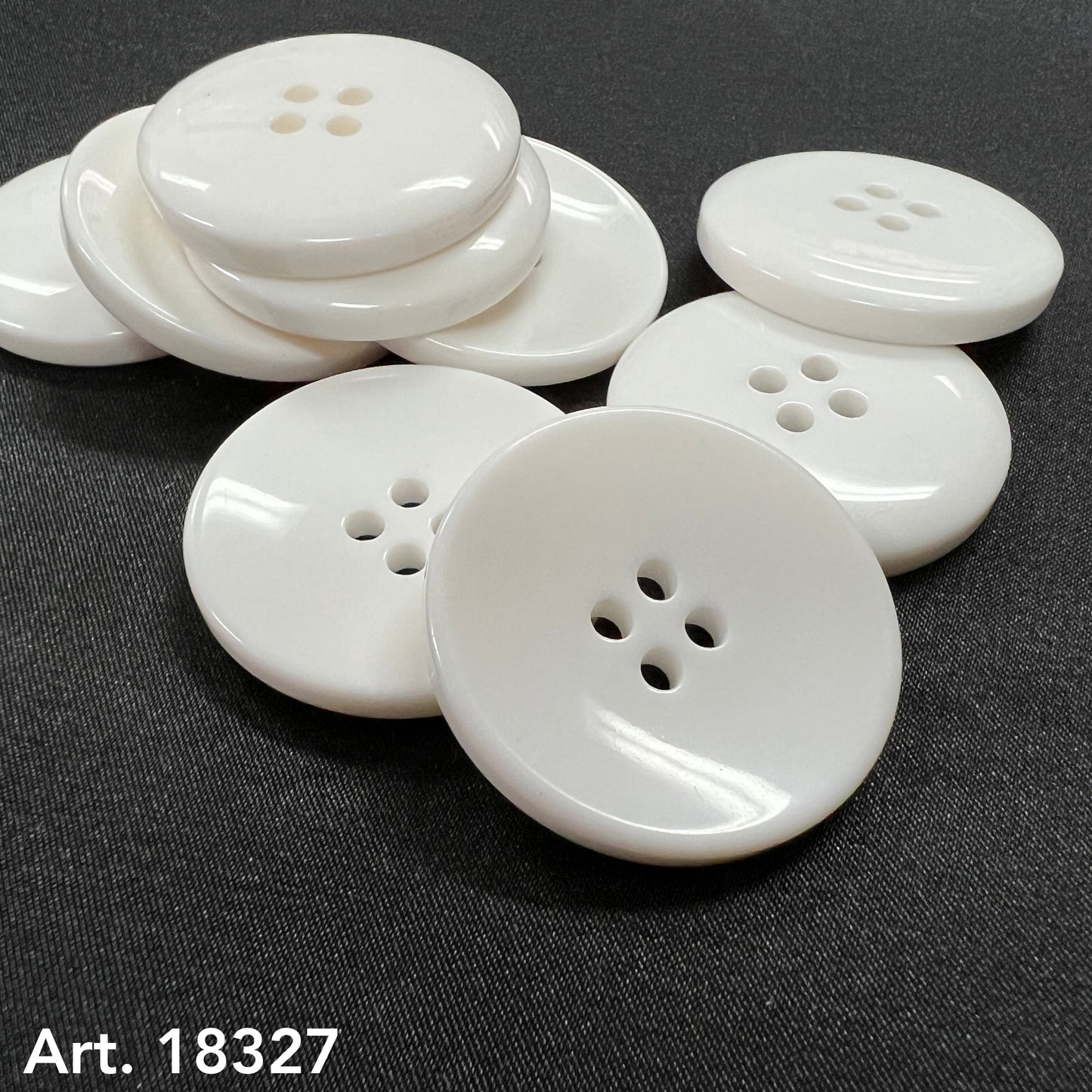 Close up of large white garment buttons by Buttonology Inc glossy four hole buttons on black fabric surface