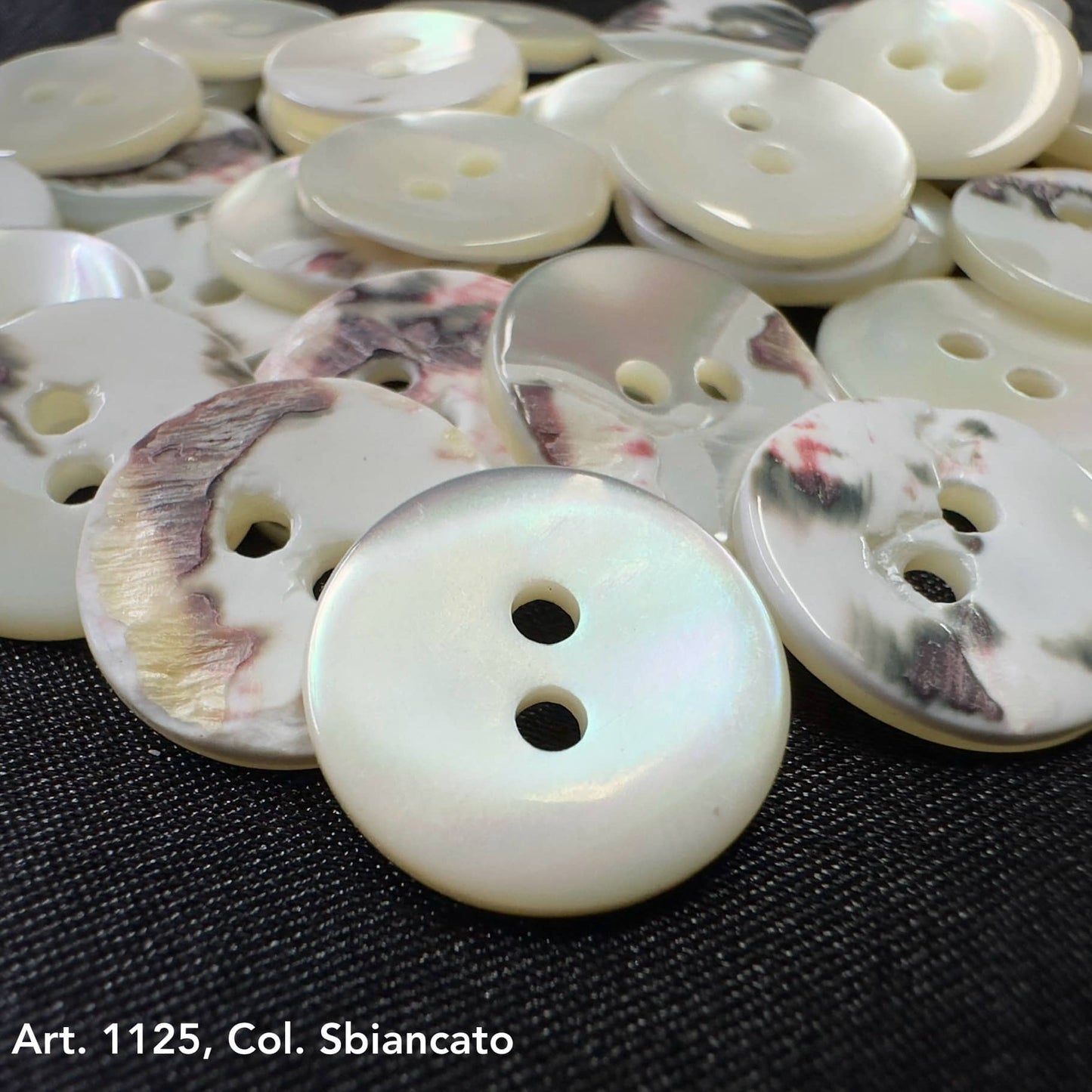 Shell buttons for sale by Buttonology Inc displayed on black fabric, showing smooth and marbled finishes