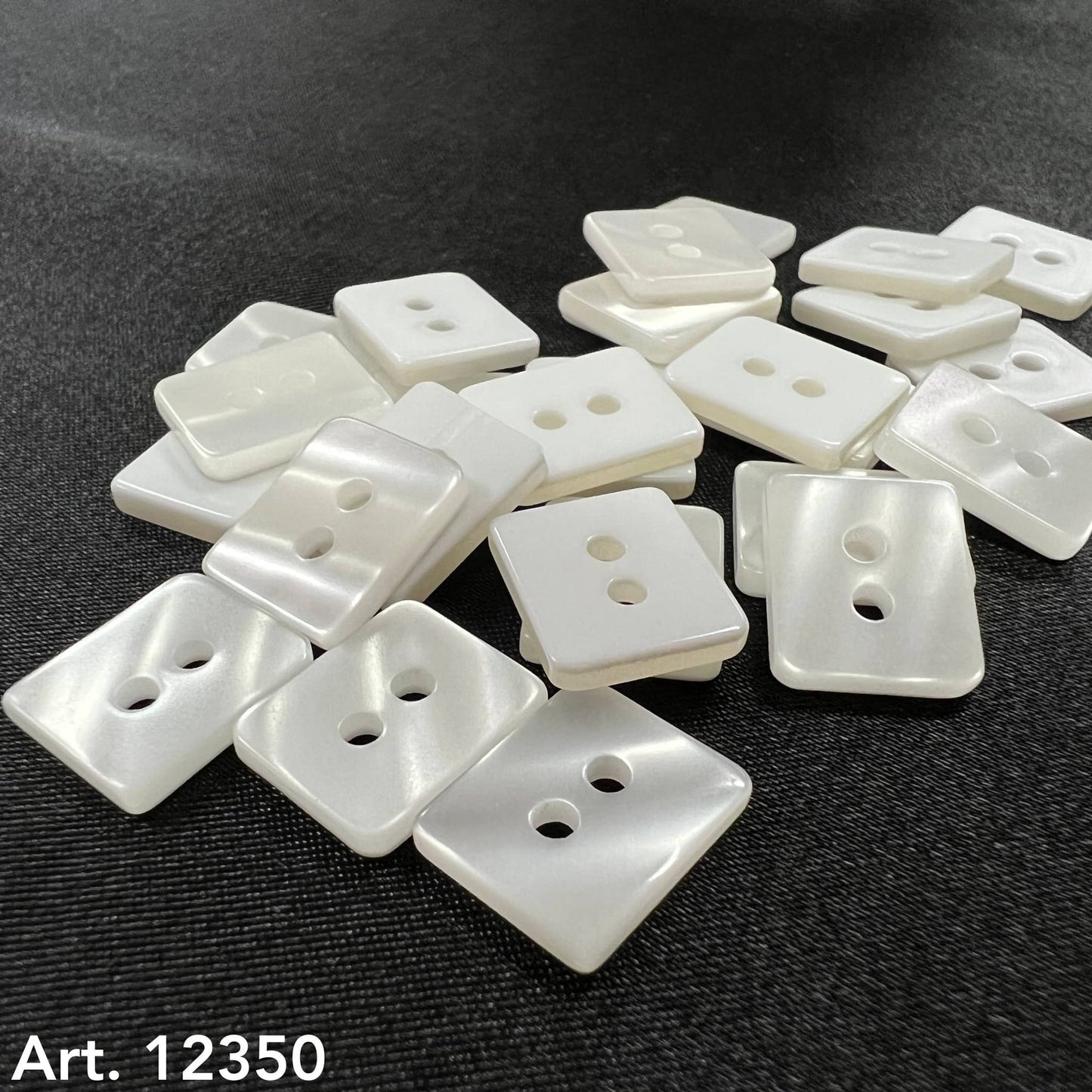 Square white buttons with two holes scattered on black fabric from Buttonology Inc