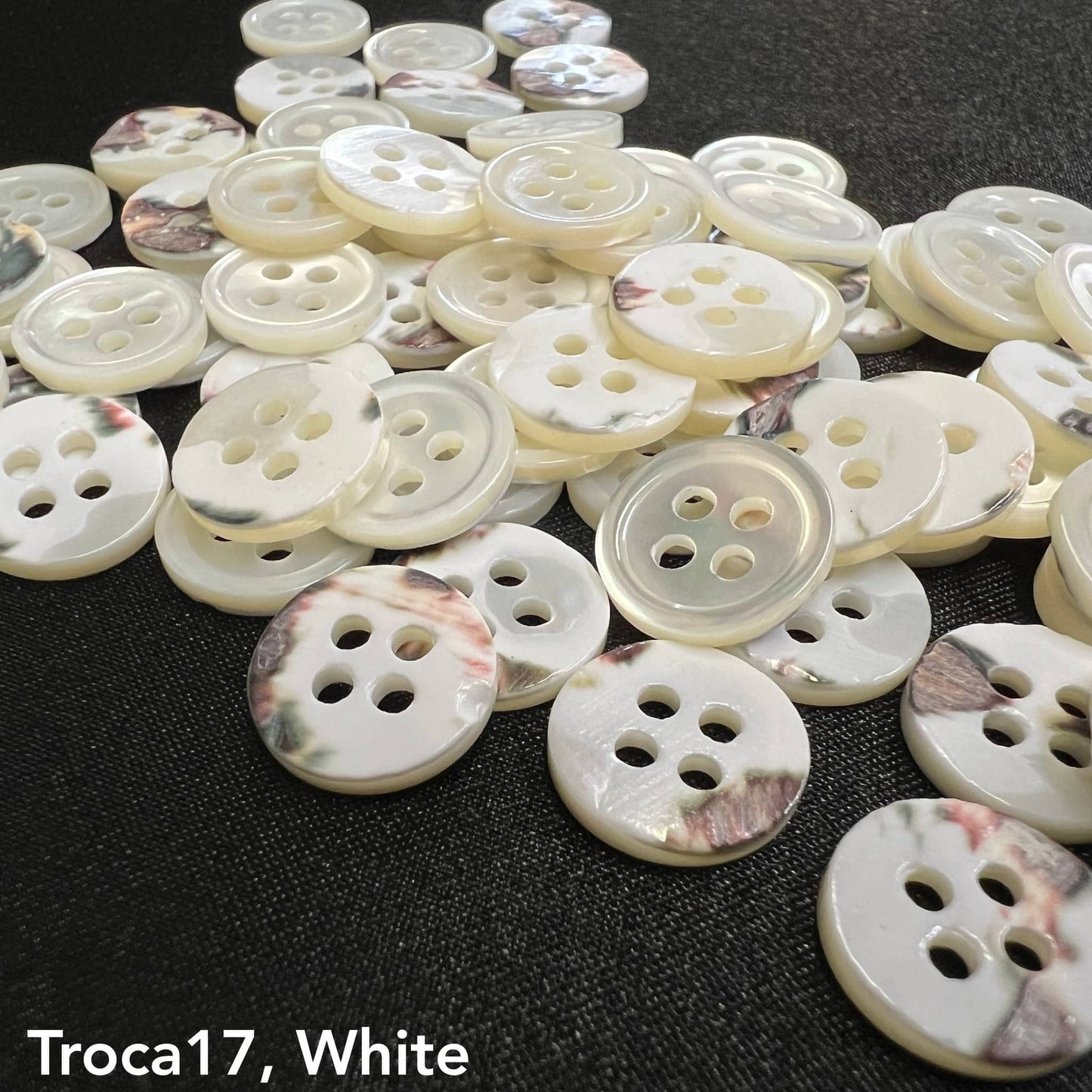 Troca shell buttons for garments in white with four holes by Buttonology Inc scattered on a black surface