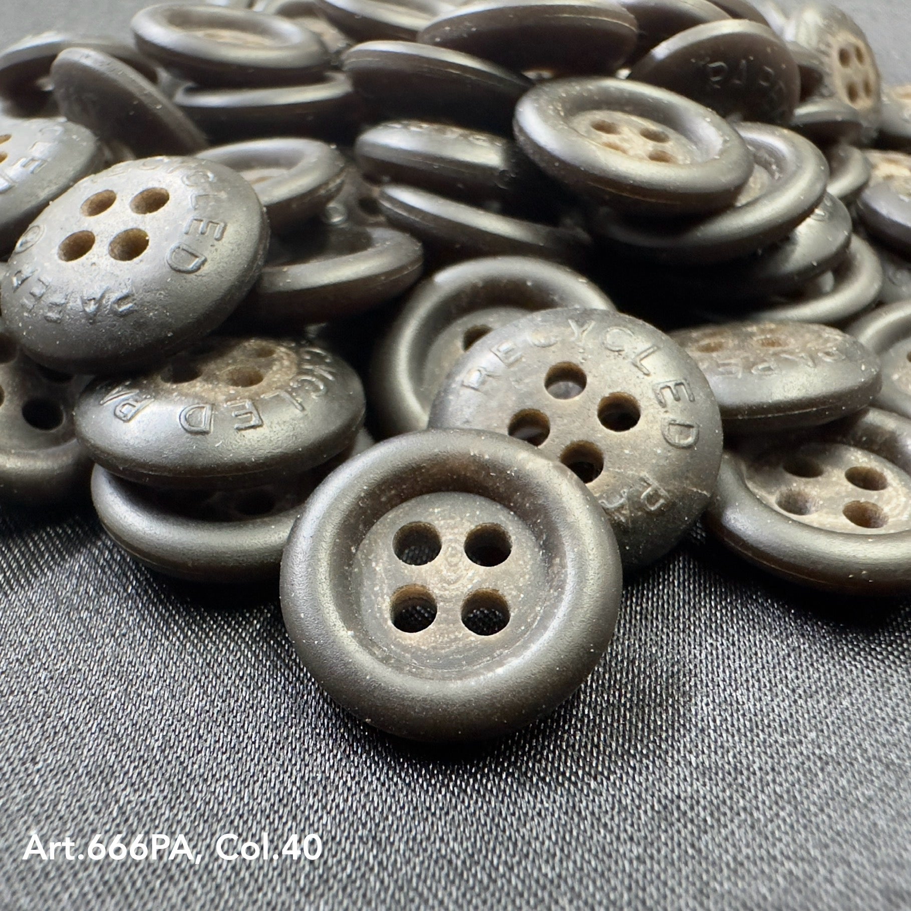 Close-up of recycled paper buttons by Buttonology Inc with four holes, dark gray color on black fabric