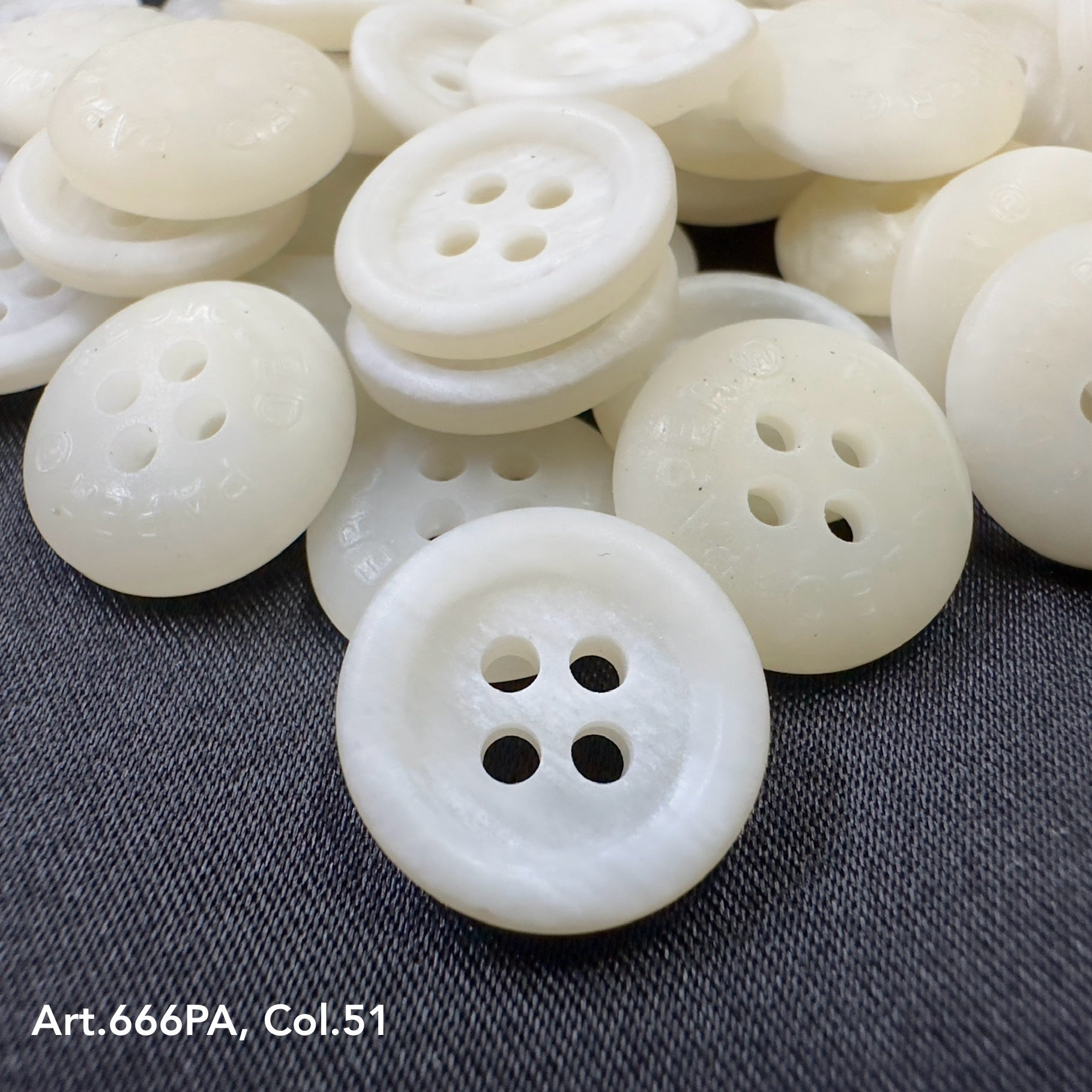 White recycled paper buttons from Buttonology Inc. with four holes on dark fabric background