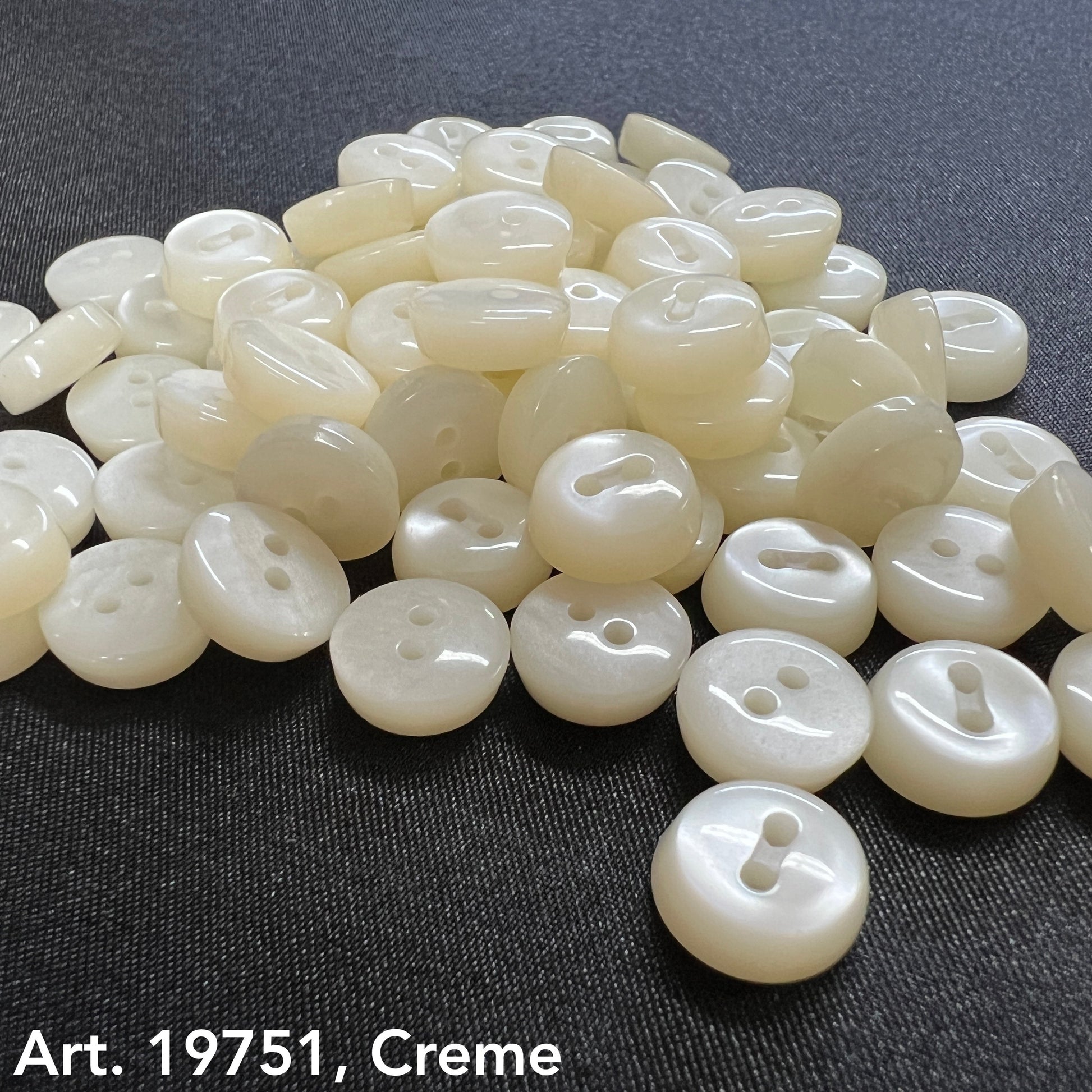 White sewing buttons for sale by Buttonology Inc in creamy white color on black fabric background