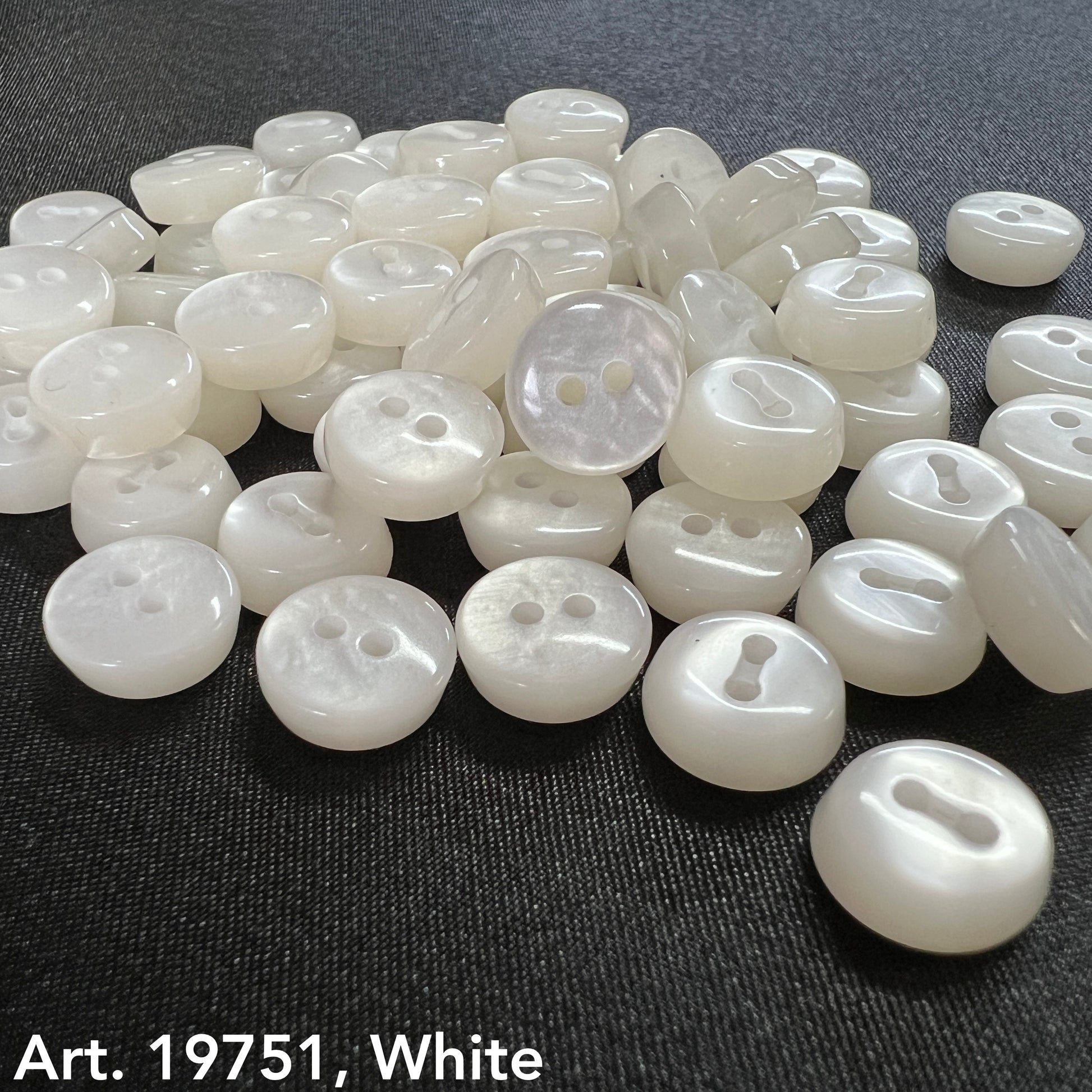White sewing buttons for sale by Buttonology Inc displayed on black fabric with smooth finish and two-hole design