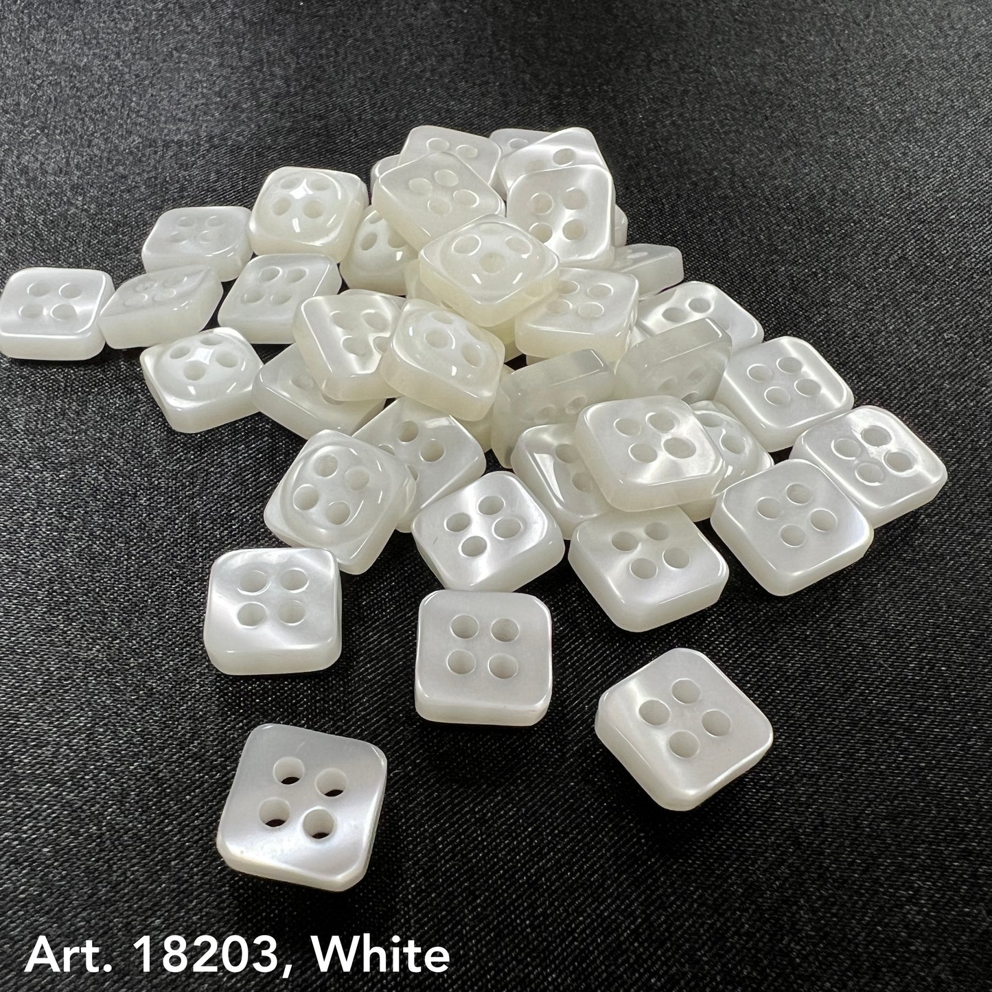 White square sewing buttons with four holes by Buttonology Inc. arranged on black fabric